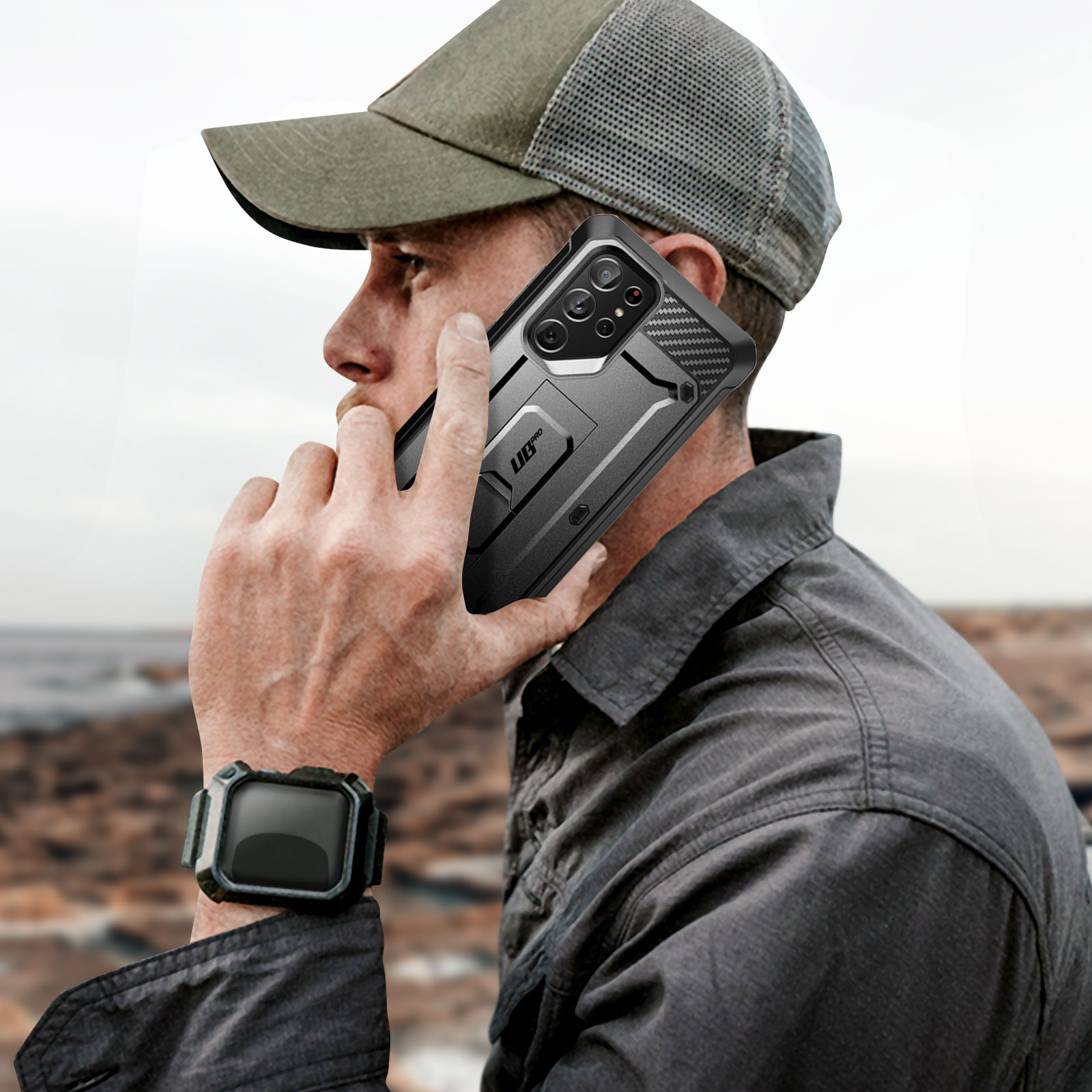 Un uomo parla al telefono con una custodia nera, indossa un berretto e un orologio al polso.