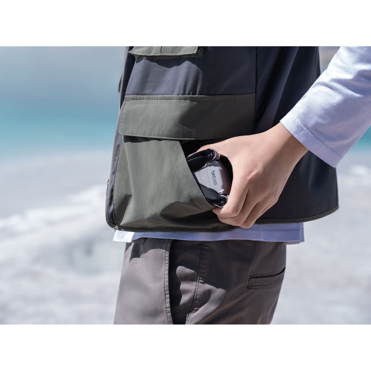 Eine Person, die eine graue Drohne in einer Tasche einer grauen Weste hält, mit verschwommenem Hintergrund.