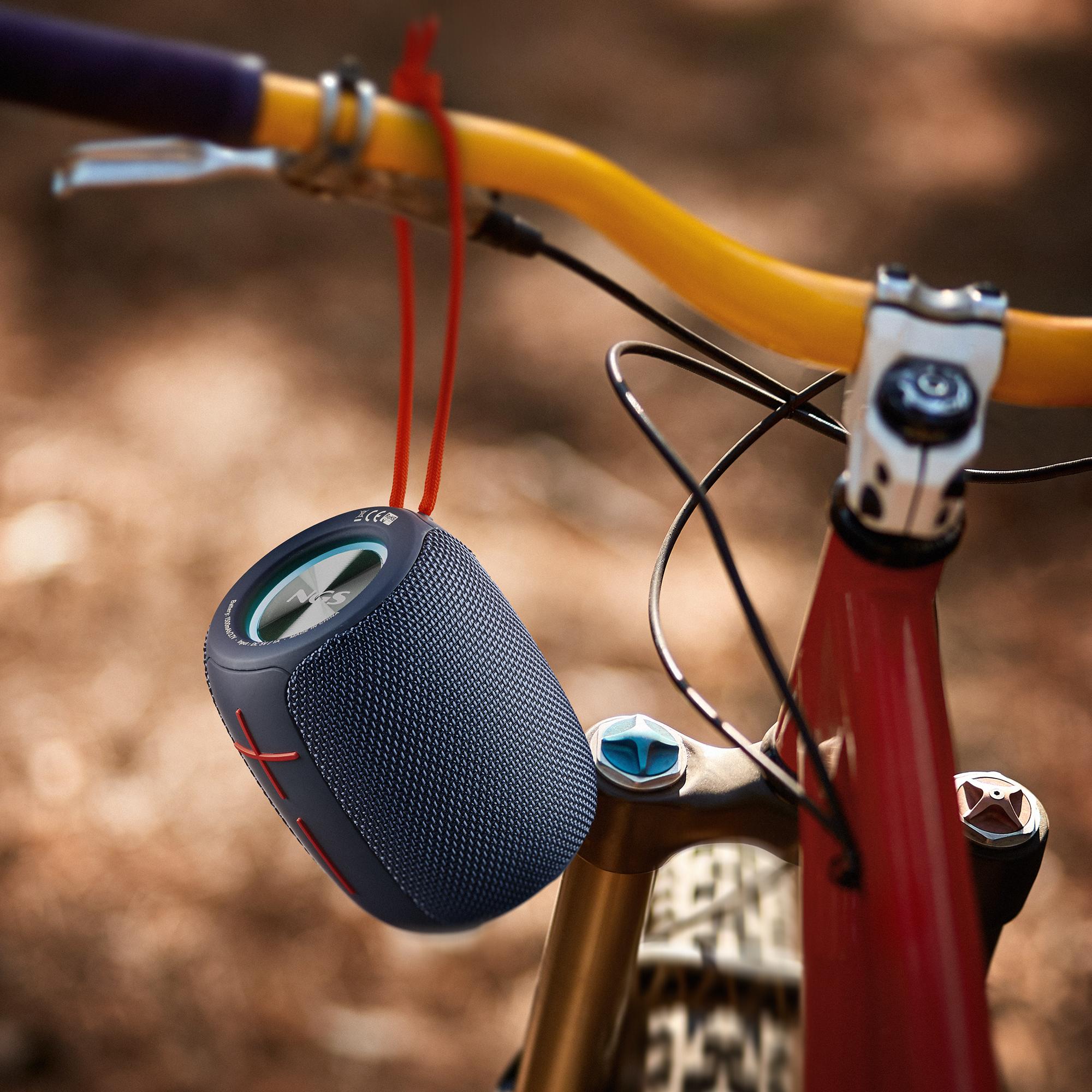 Czarny i niebieski głośnik wisi na rowerze. Widoczne czerwone akcenty i żółta kierownica.