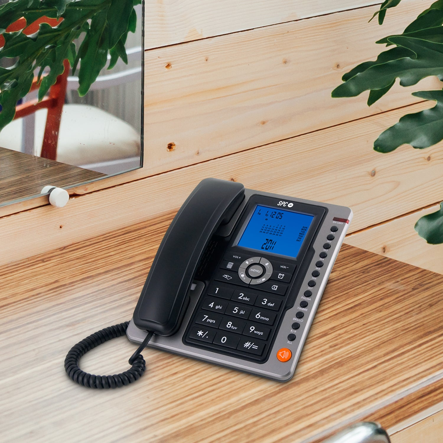 Telefono fisso nero su una scrivania di legno, con display e riflesso nello specchio.