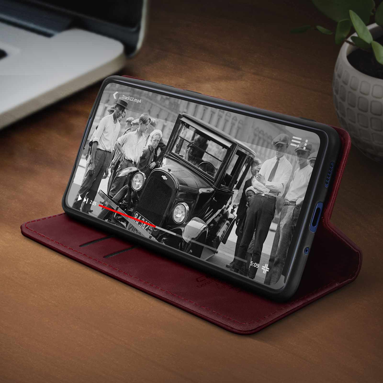 Ein Telefon in einer roten Lederhülle zeigt einen Schwarzweißfilm mit einem Auto und Personen.