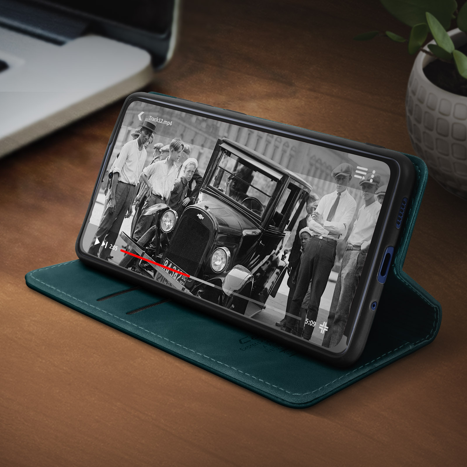Ein Telefon in einer türkisfarbenen Hülle auf einem Holztisch. Der Bildschirm zeigt eine Schwarz-Weiß-Filmszene.