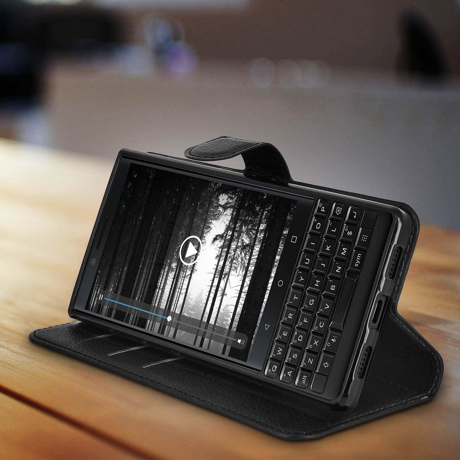 Eine schwarze Handyhülle mit Tastatur. Ein Telefon ist darin, das ein Video mit einer Waldszene zeigt.