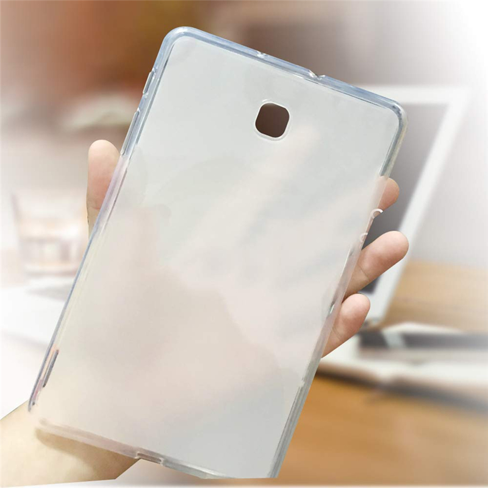Eine Hand, die eine transparente Tablet-Hülle hält, mit verschwommenem Laptop-Hintergrund.