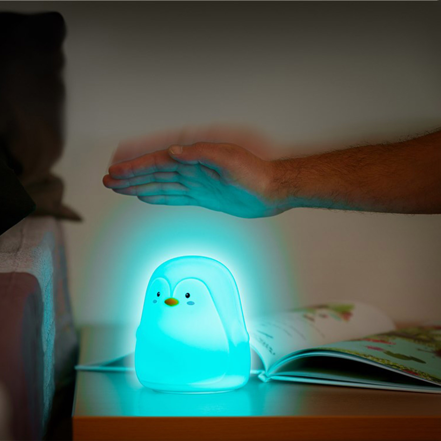 Eine pinguinförmige Lampe, die blaues Licht aussendet. Eine Hand schwebt über ihr in der Nähe eines offenen Buches.
