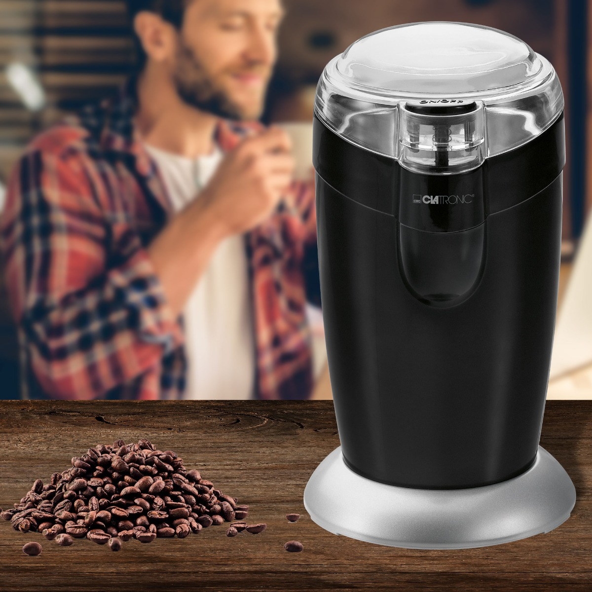 Czarny młynek do kawy z ziarnami kawy na drewnianym stole. Rozmyty mężczyzna w tle.