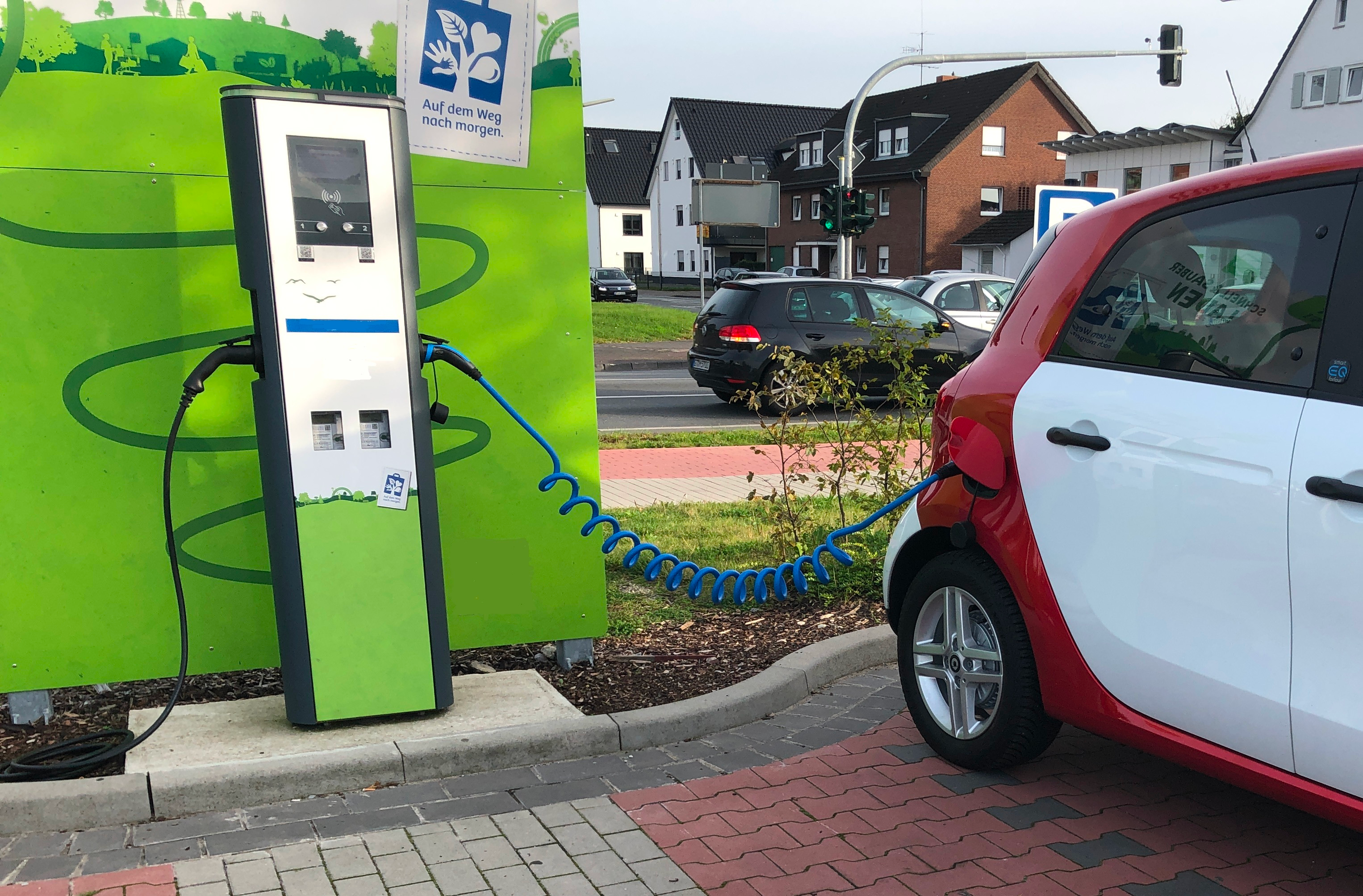 Elektroauto lädt. Ein rot-weißes Auto ist an einer Ladestation angeschlossen. Grüner Hintergrund.