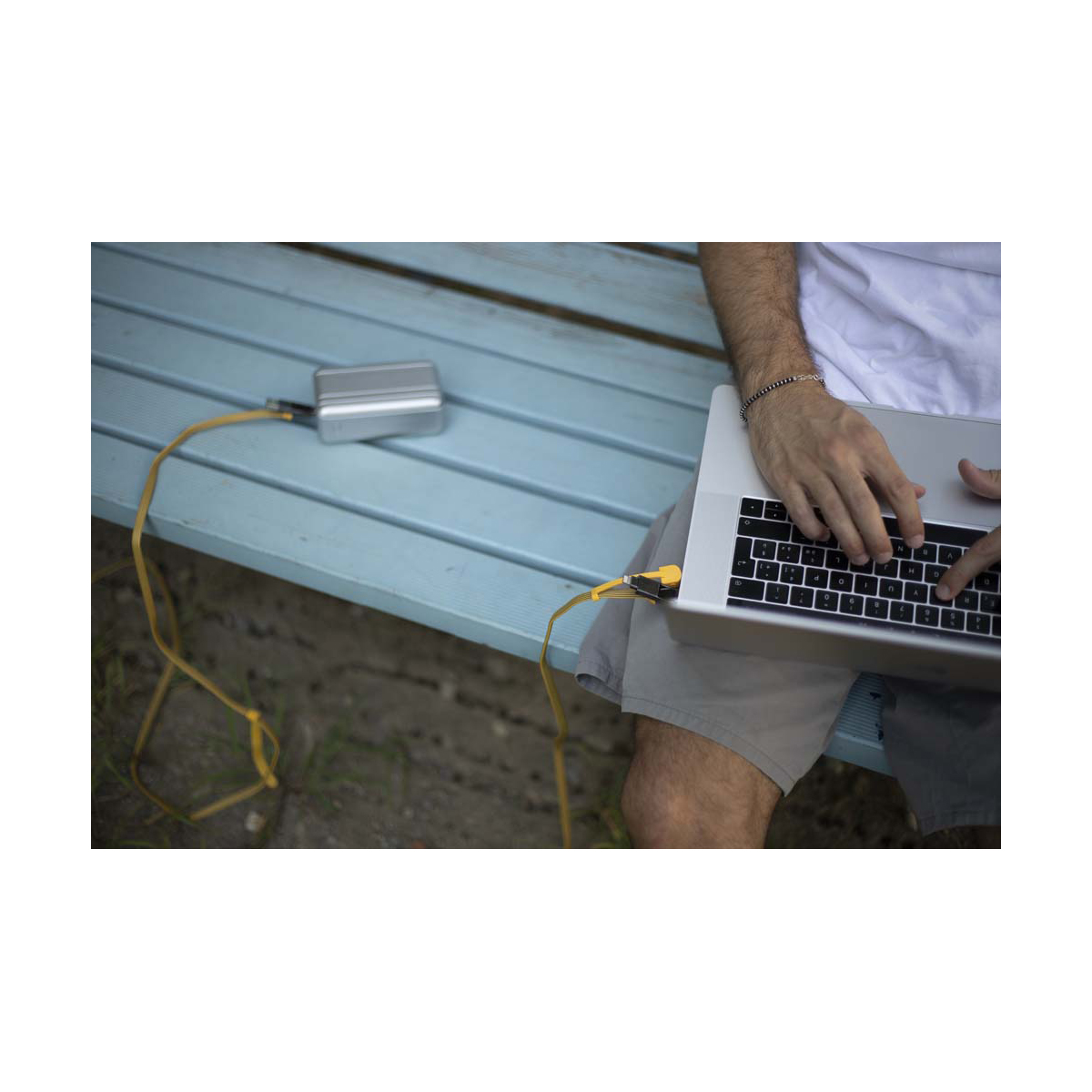 Une personne utilisant un ordinateur portable, connecté à une batterie externe argentée via un câble jaune.