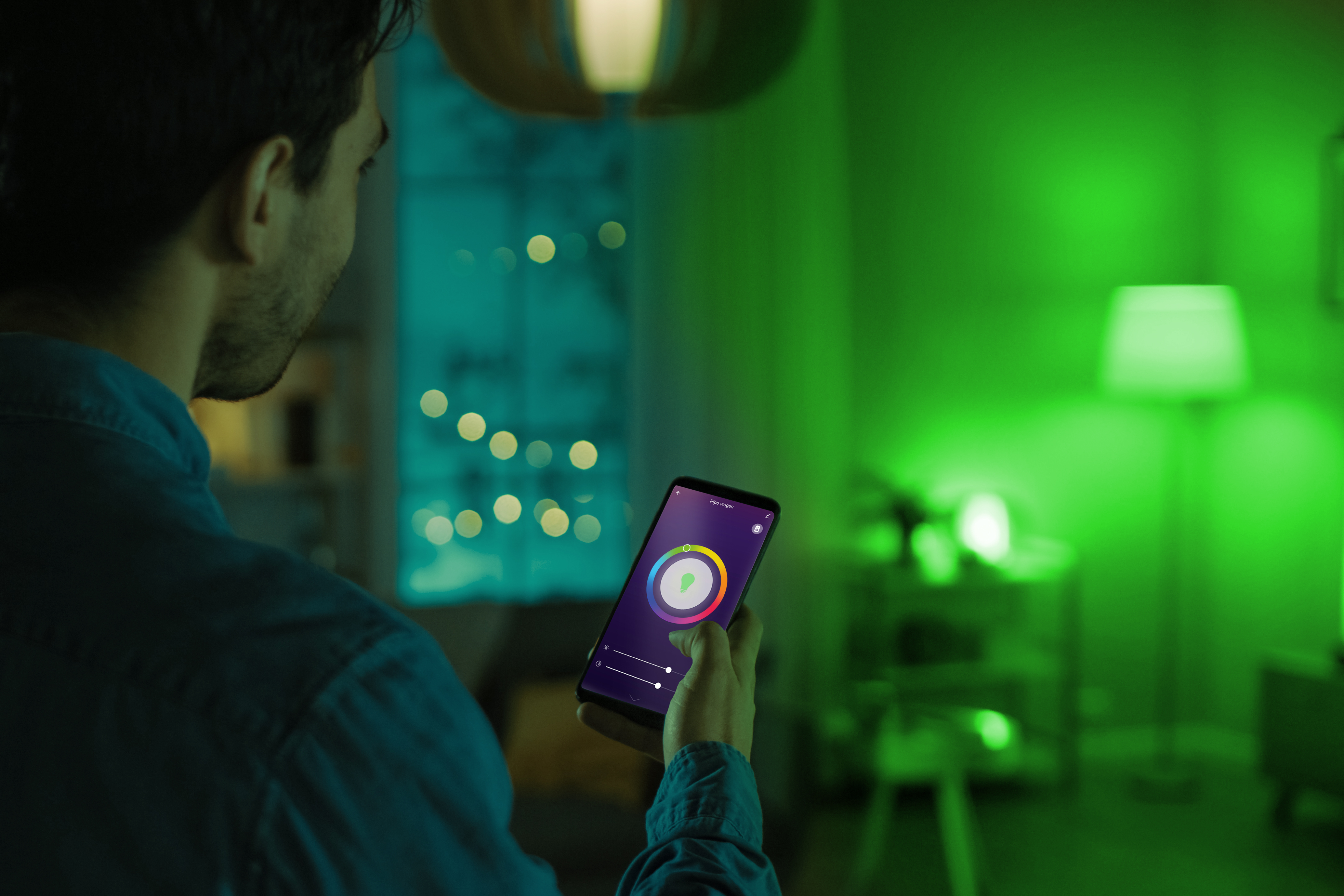 Mężczyzna trzyma telefon z aplikacją do kontroli pokoju. Pokój jest oświetlony na zielono.