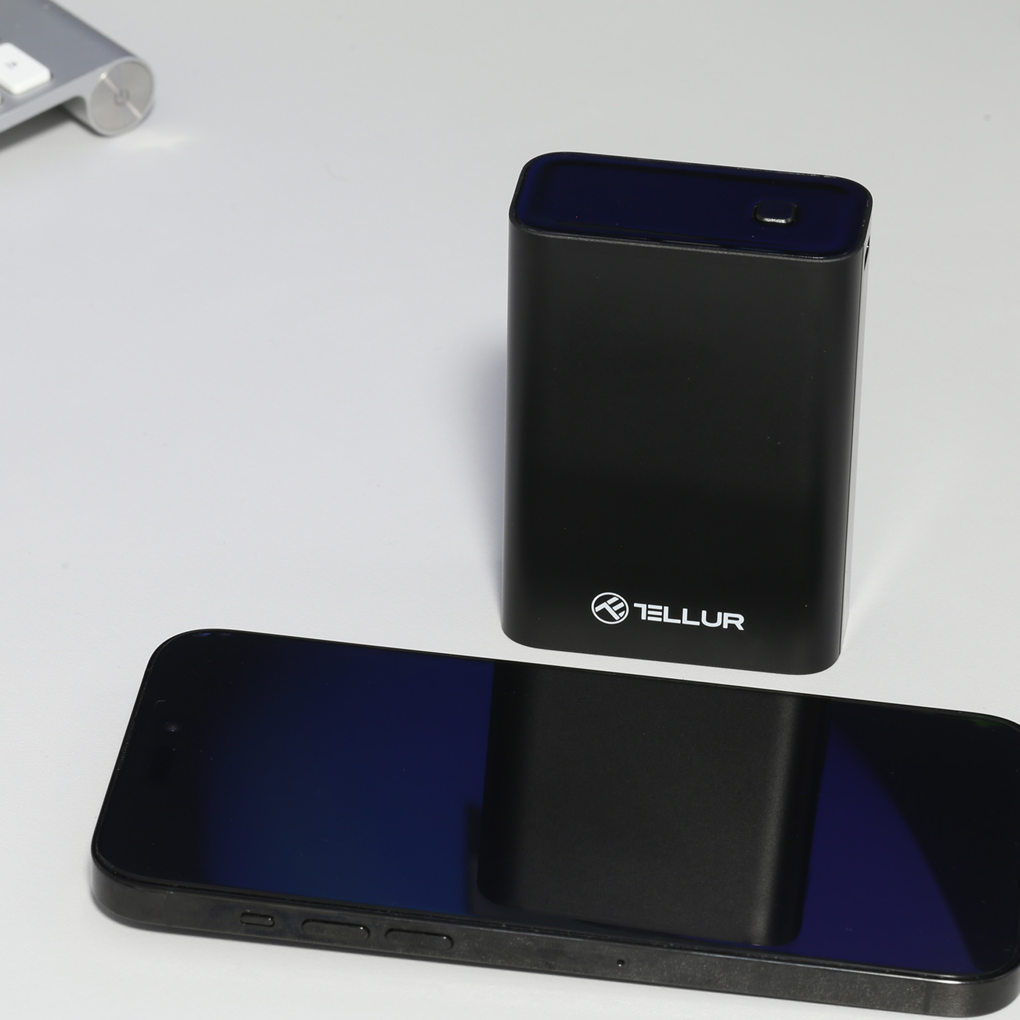 Czarna przenośna ładowarka obok czarnego smartfona na białej powierzchni.