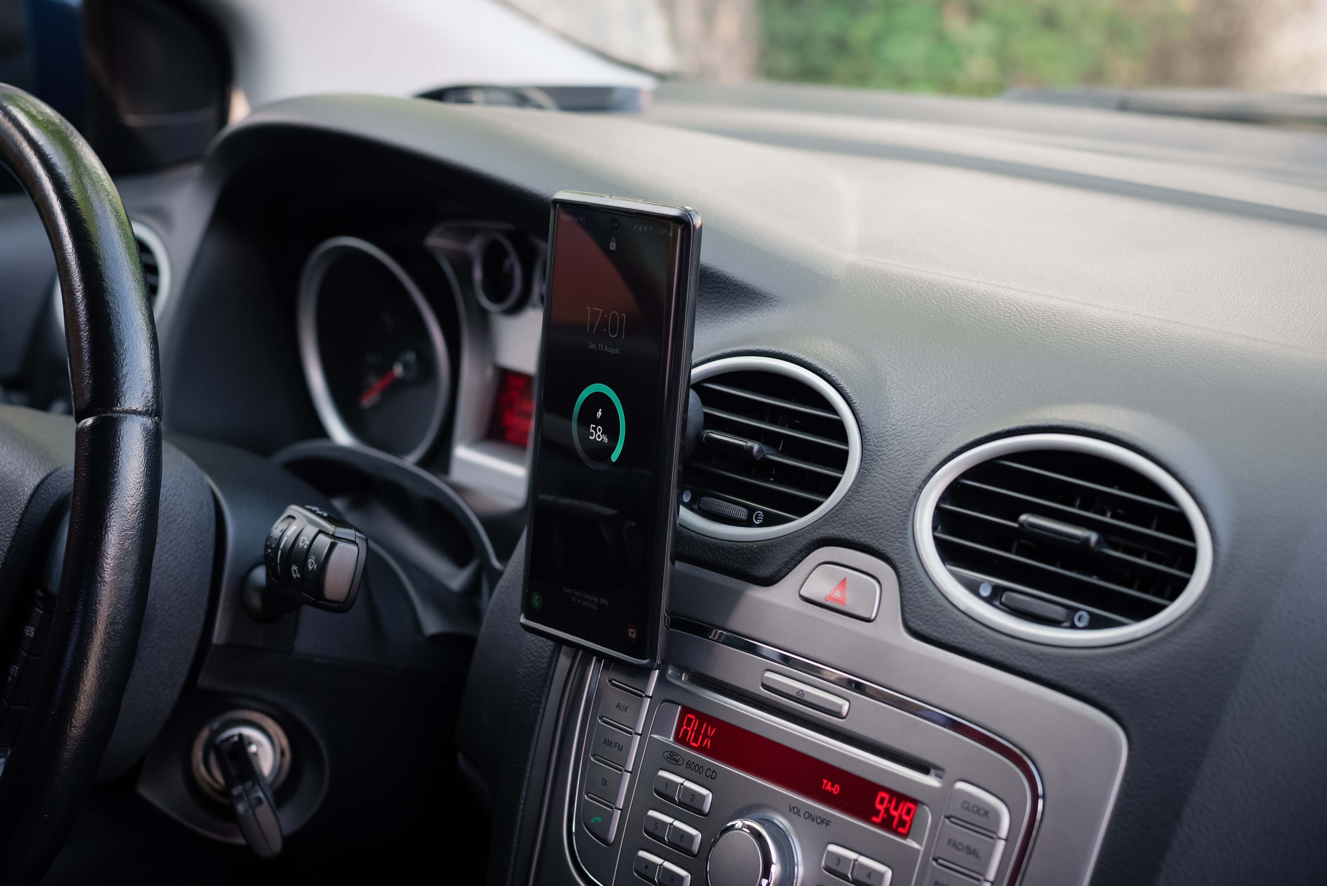 Smartfon zamontowany na desce rozdzielczej samochodu, wyświetlający status ładowania.