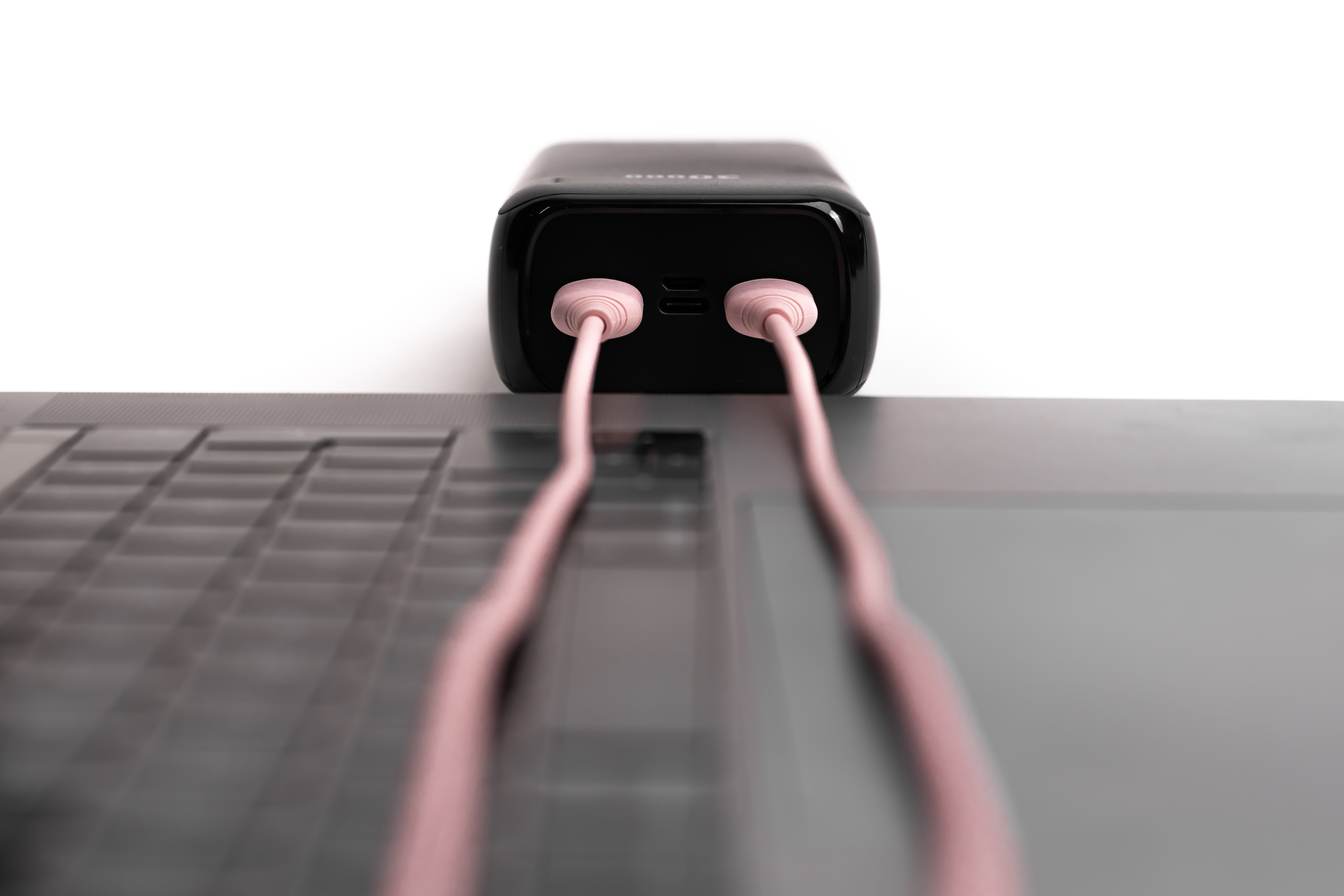 Czarny power bank z różowymi przewodami podłączonymi do laptopa. Białe tło.