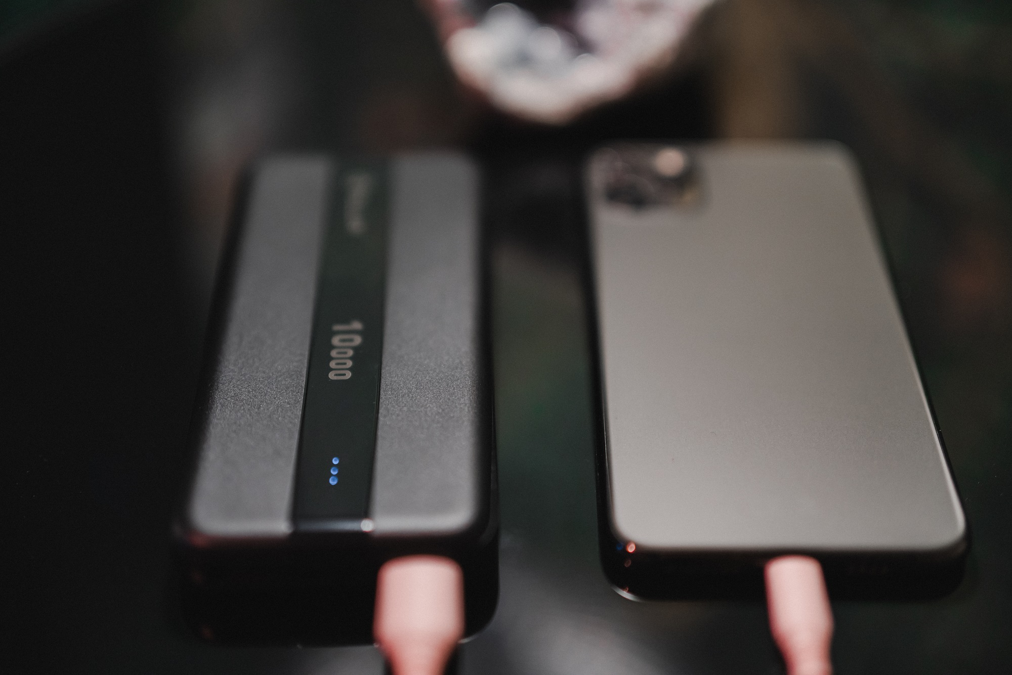 Czarny power bank obok telefonu, oba połączone za pomocą różowych kabli ładujących. Power bank pokazuje 10000.