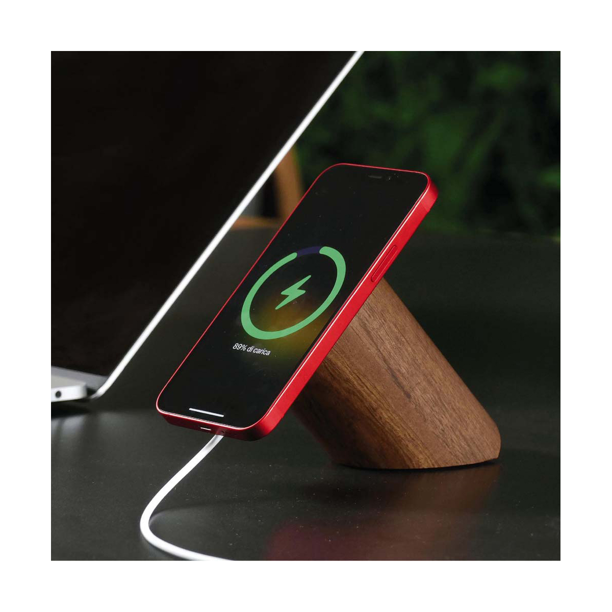 Rotes Telefon auf einem Holzständer, das aufgeladen wird. Telefon zeigt Ladesymbol. Weißes Kabel und Hintergrund.