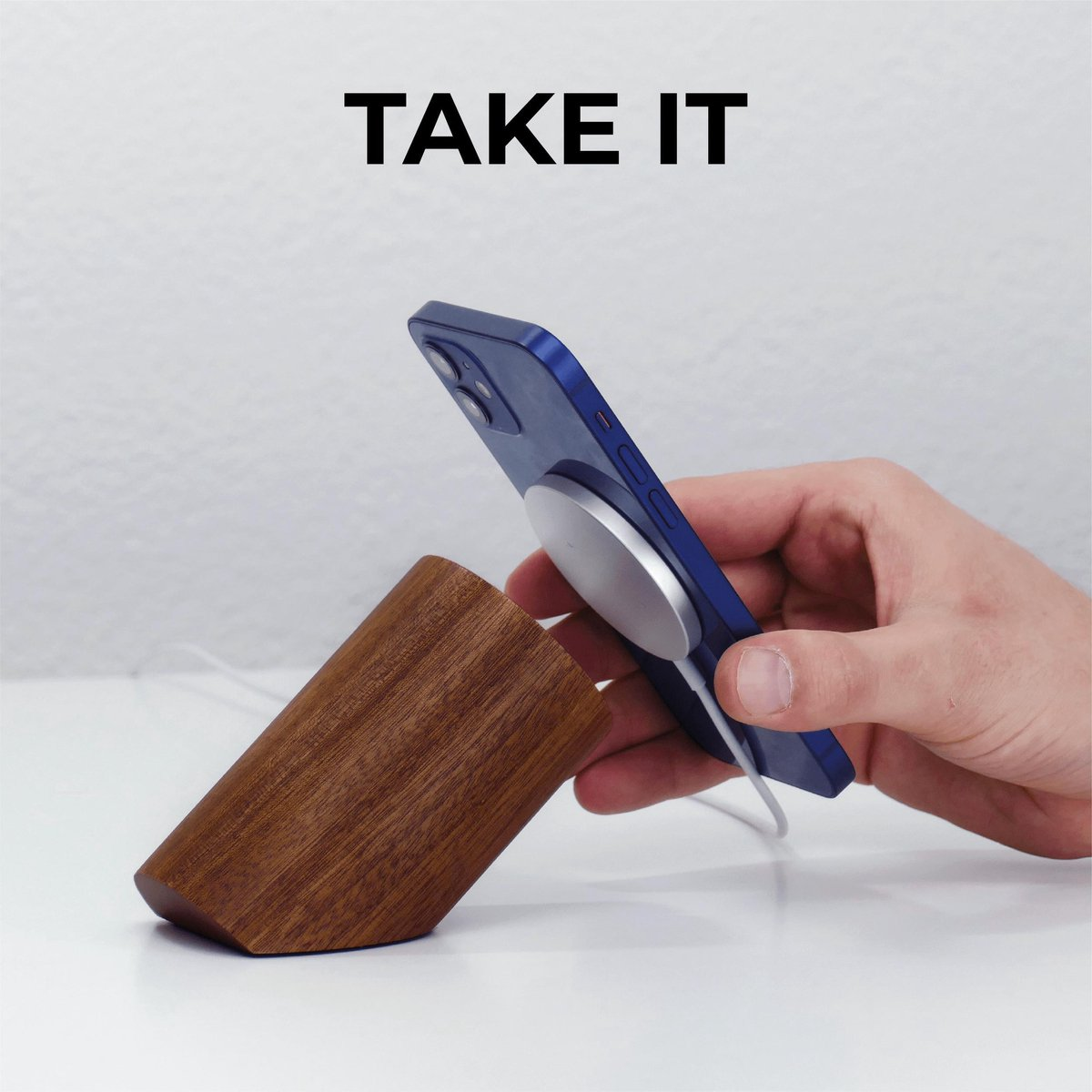 Eine Hand hält ein blaues Telefon mit einem magnetischen Ladegerät neben einem Holzständer. Weißer Hintergrund.