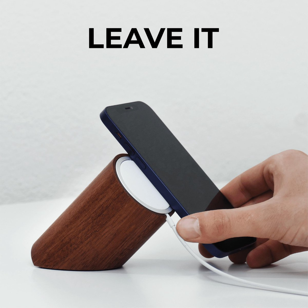 Hand, die ein Telefon auf einem drahtlosen Holzladegerät auflädt. Text: "LEAVE IT".