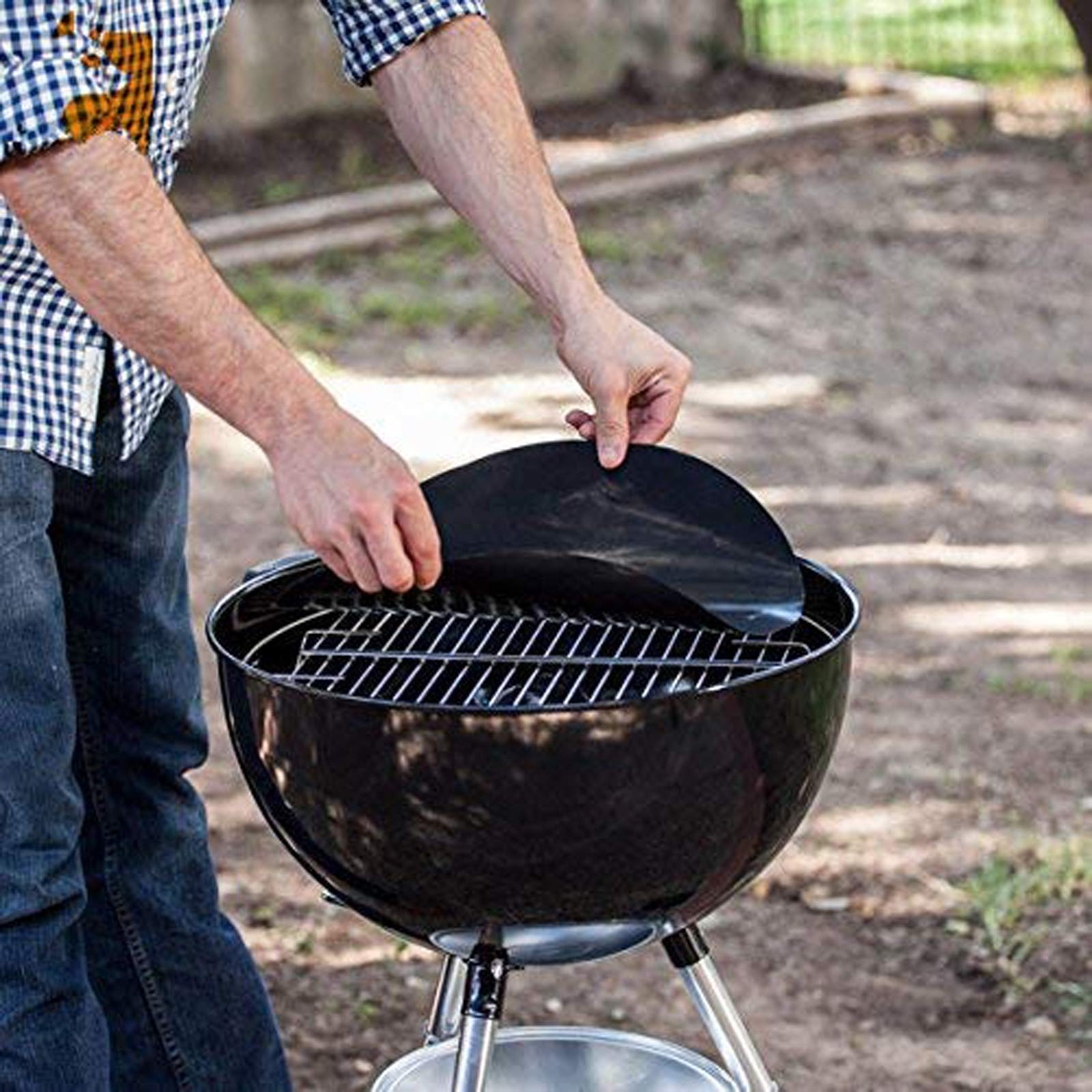 Eine Person legt eine schwarze Grillmatte auf einen schwarzen Holzkohlegrill. Die Szene ist im Freien.