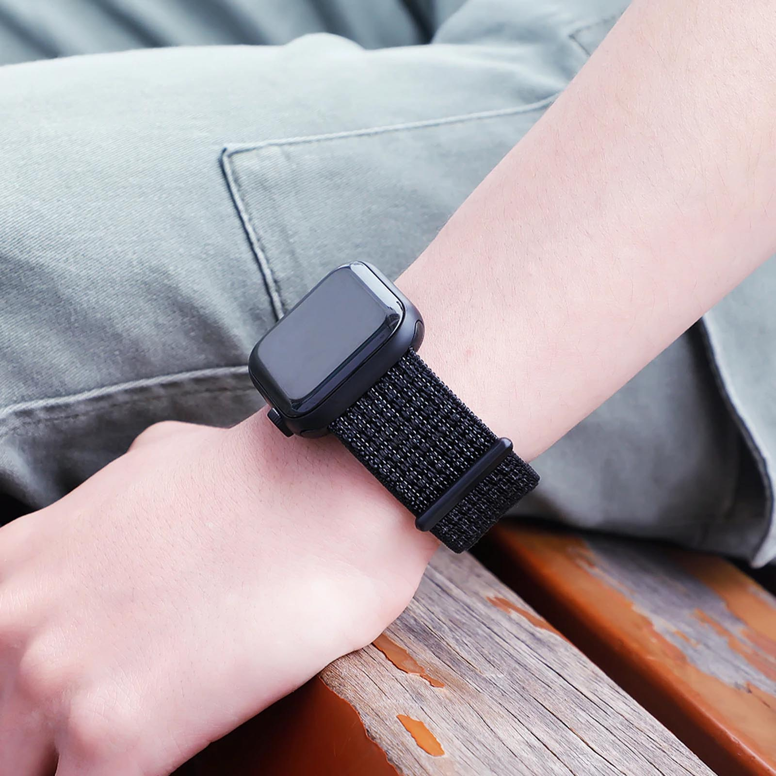 Muñeca de una persona con reloj inteligente negro y banda de tela negra sobre superficie de madera.