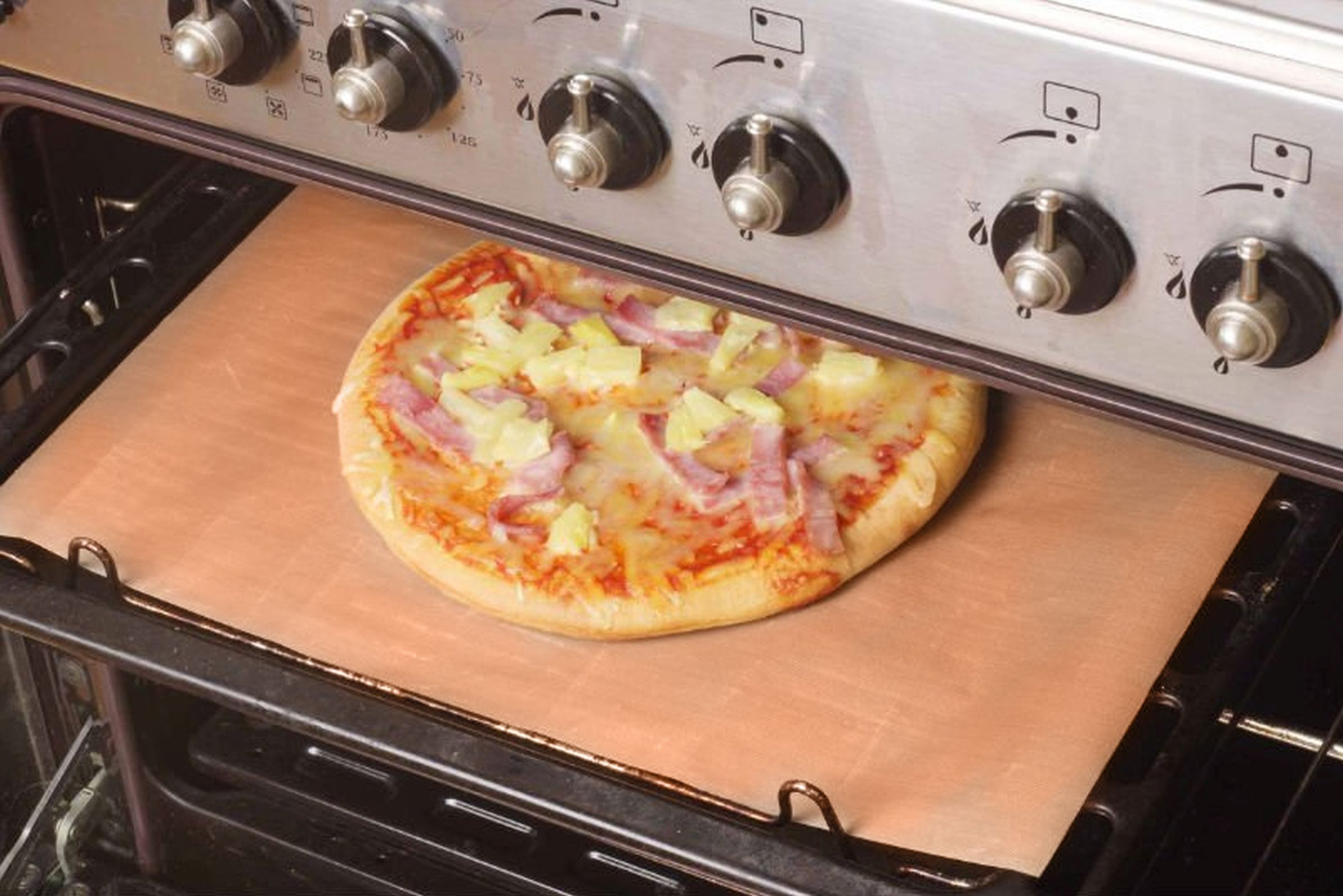 Eine Pizza mit Ananas und Schinken in einem Ofen auf einem Backblech.