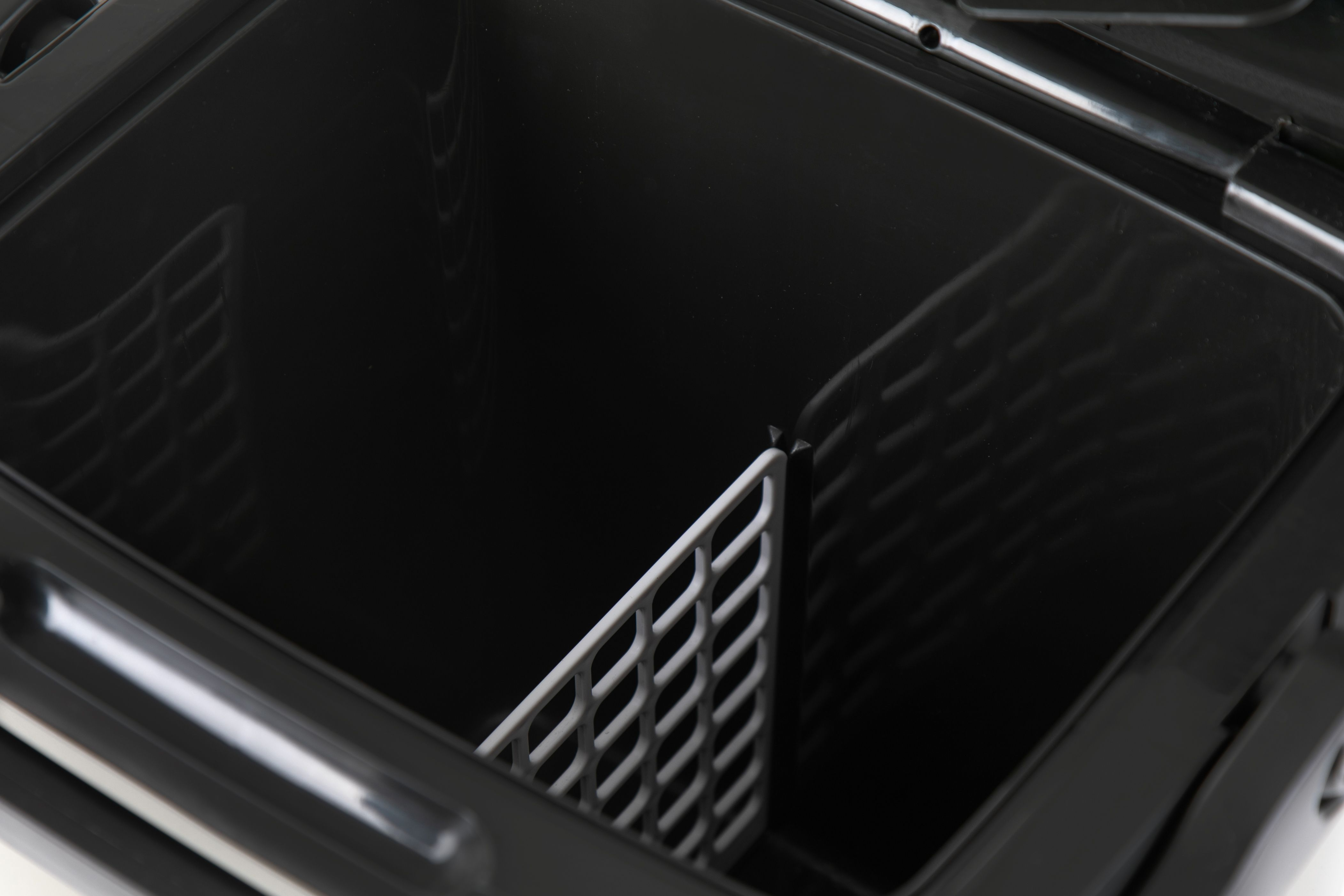 Eine offene schwarze Kühlbox mit weißem Trenner darin, auf weißem Untergrund.
