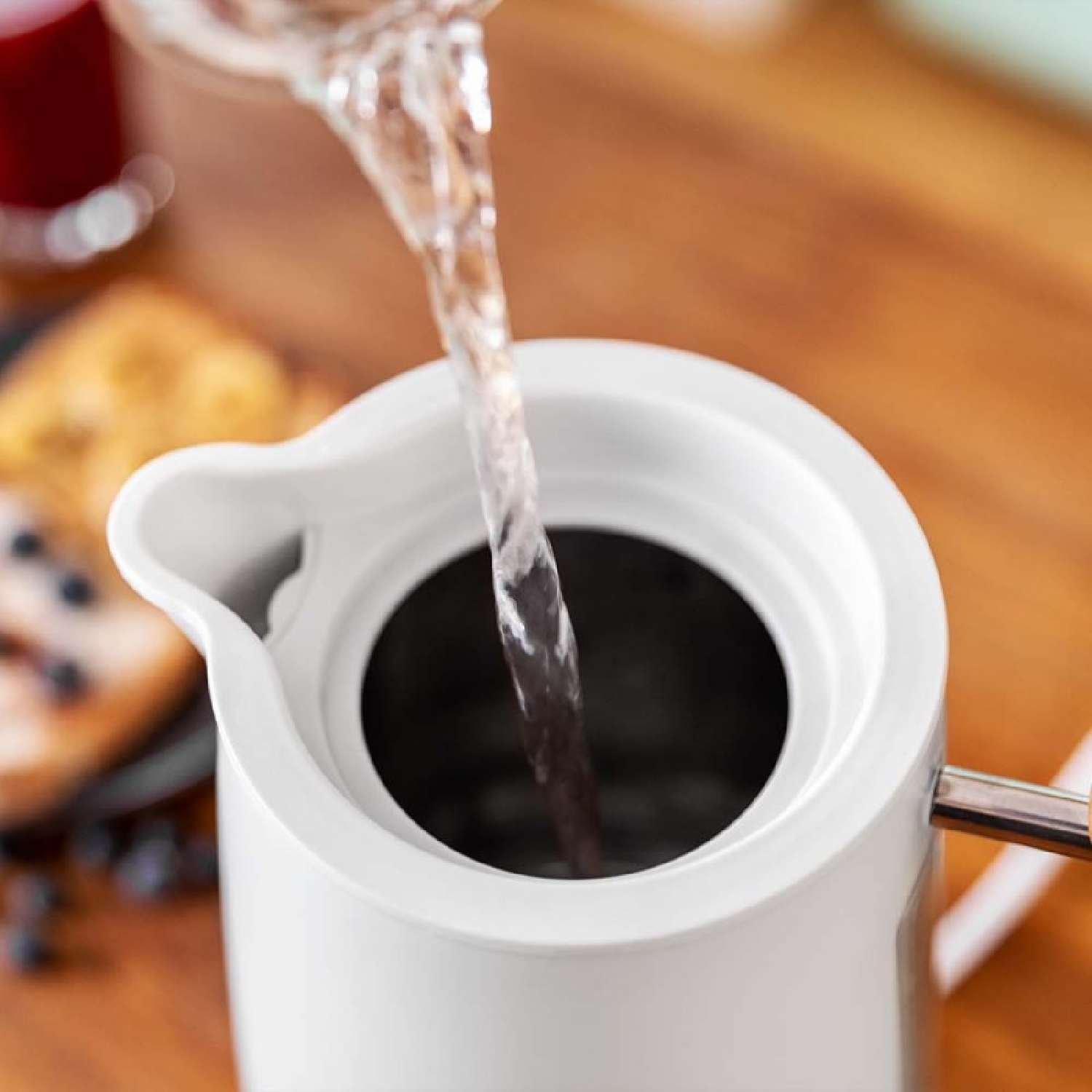 Woda wlewana do białego czajnika, z rozmytym tłem.