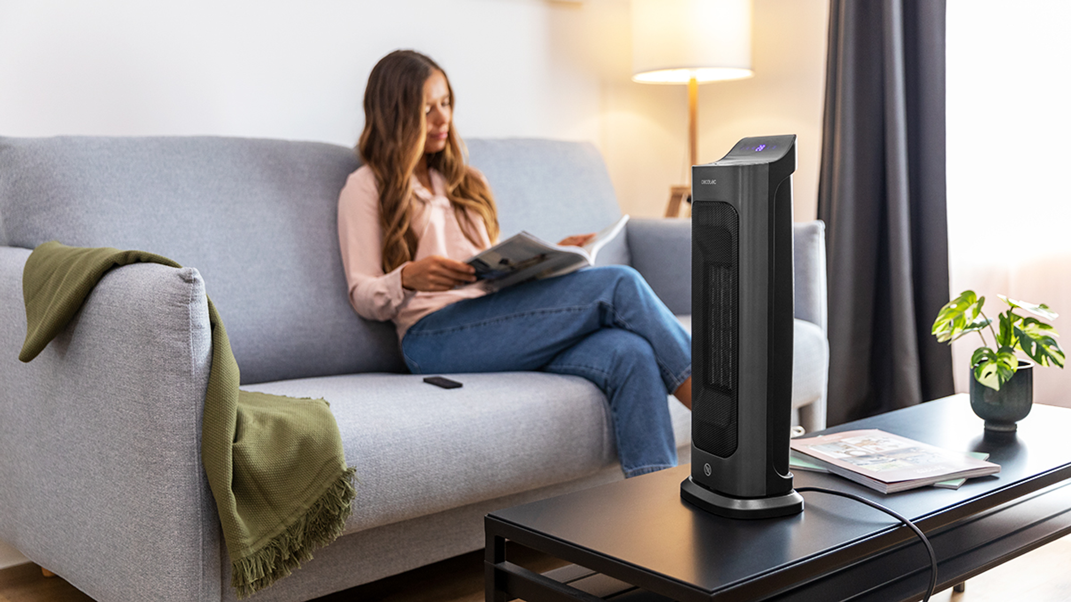 Kobieta czyta czasopismo na szarej sofie z czarnym grzejnikiem w pobliżu.