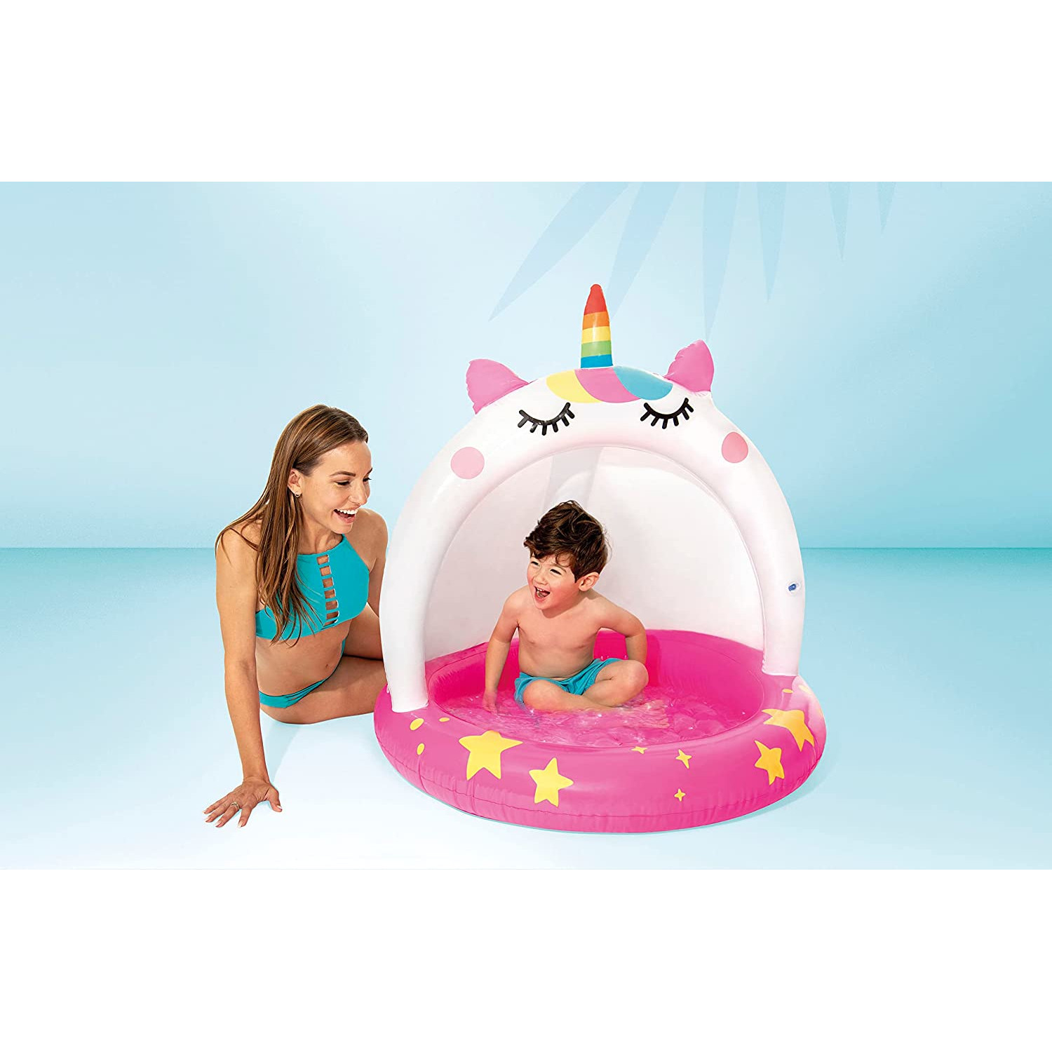 Frau und Kind in einem aufblasbaren Einhorn-Pool. Der Pool hat Sterne und ein Regenbogen-Einhorn.