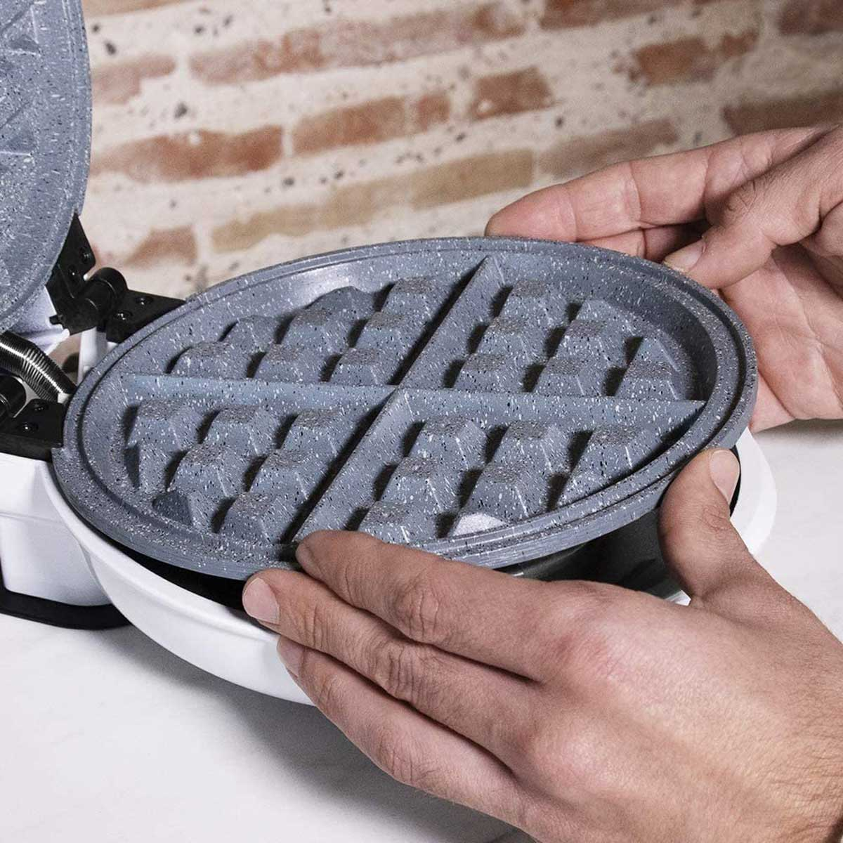 Hände halten ein Waffeleisen und zeigen die Kochplatten. Die Platten sind grau und haben ein Gittermuster.