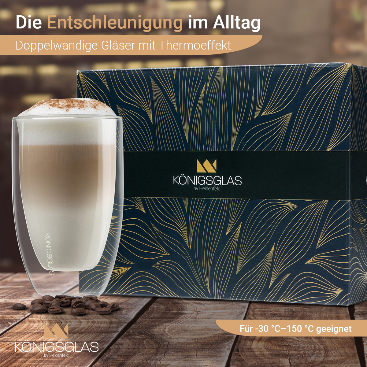 Doppelwandiges Glas mit Kaffee. Box-Set mit Goldblatt-Design und Text auf Deutsch. Kaffeebohnen im Vordergrund.