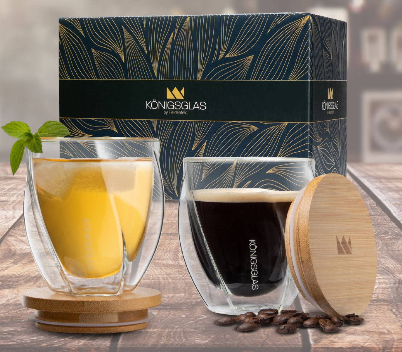 Zwei Gläser Kaffeegetränke, eines mit Schaum, neben einer Geschenkbox und Kaffeebohnen auf einem Holztisch.