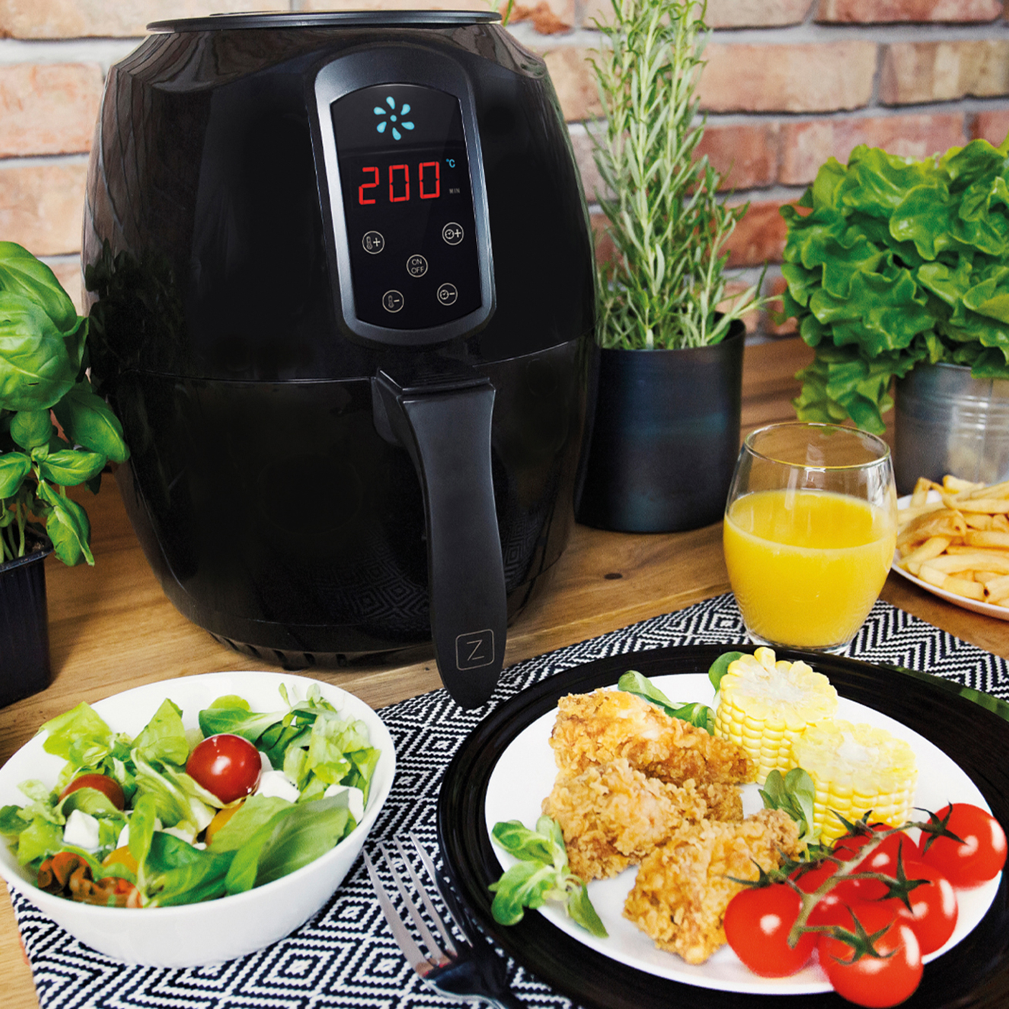 Czarna frytkownica powietrzna z jedzeniem na blacie, w tym sałatką, smażonym kurczakiem i kukurydzą.