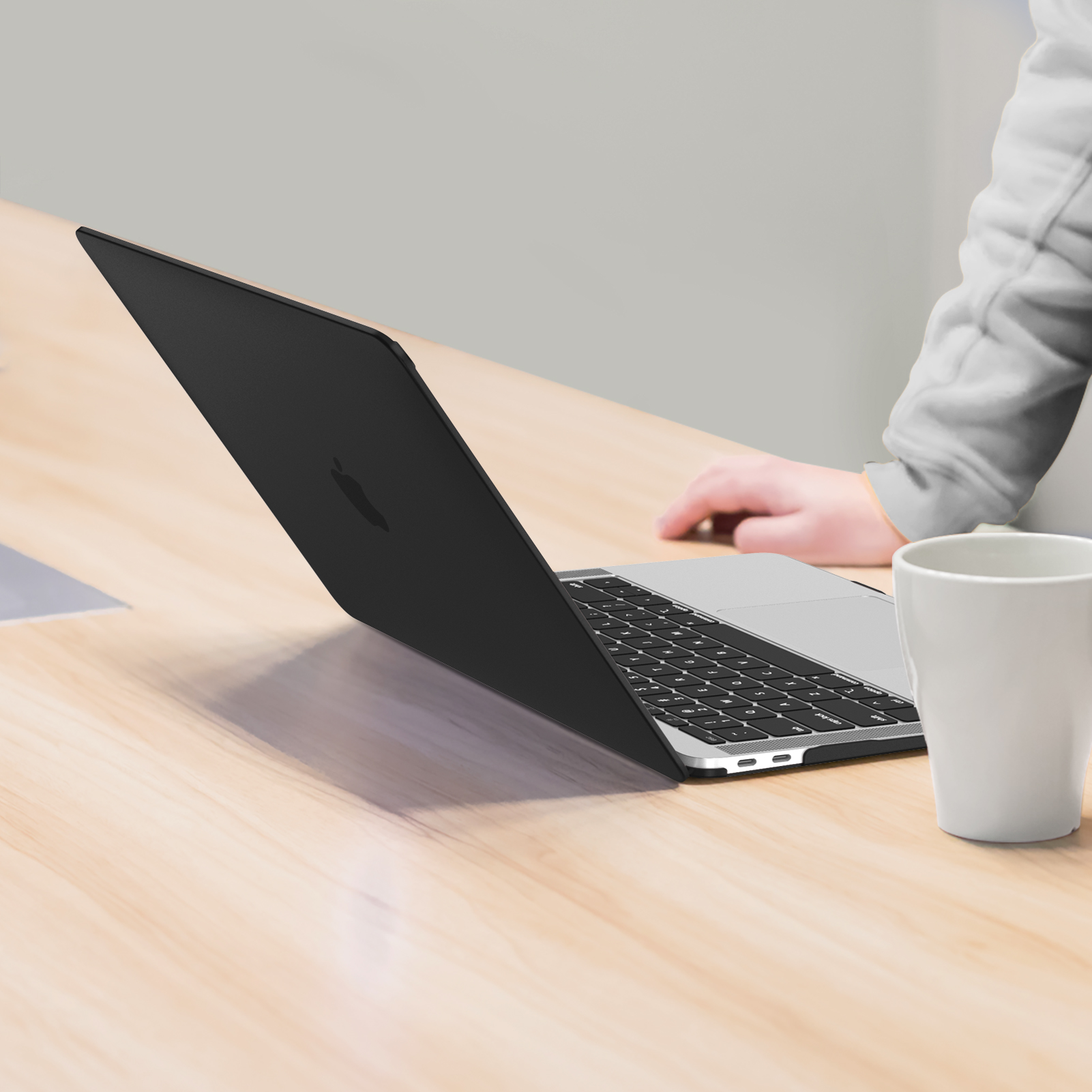 Schwarzer Laptop auf Holzschreibtisch, mit weißem Becher. Arm im Hintergrund.