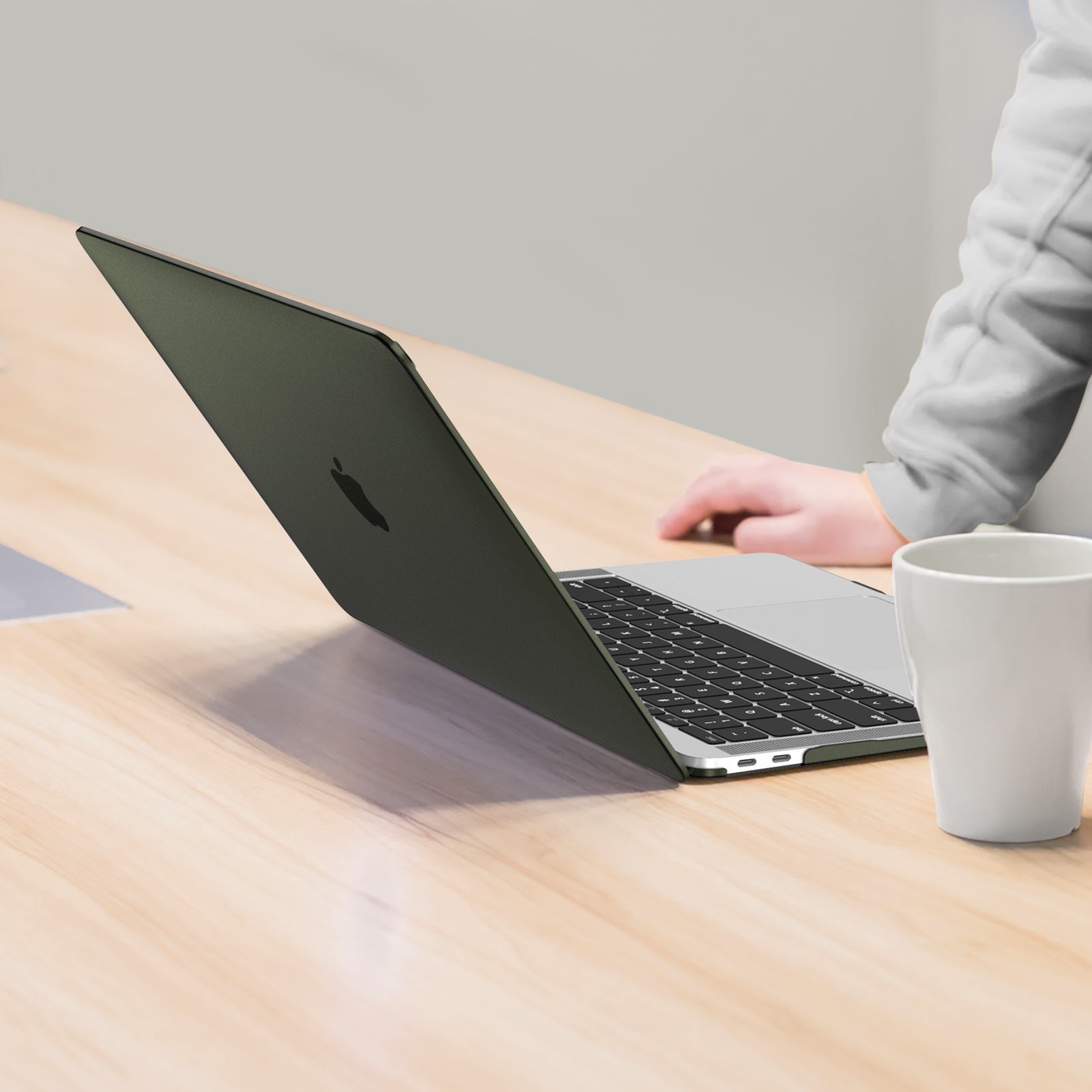 Laptop auf einem Schreibtisch, geöffnet, mit Arm einer Person und weißem Becher.