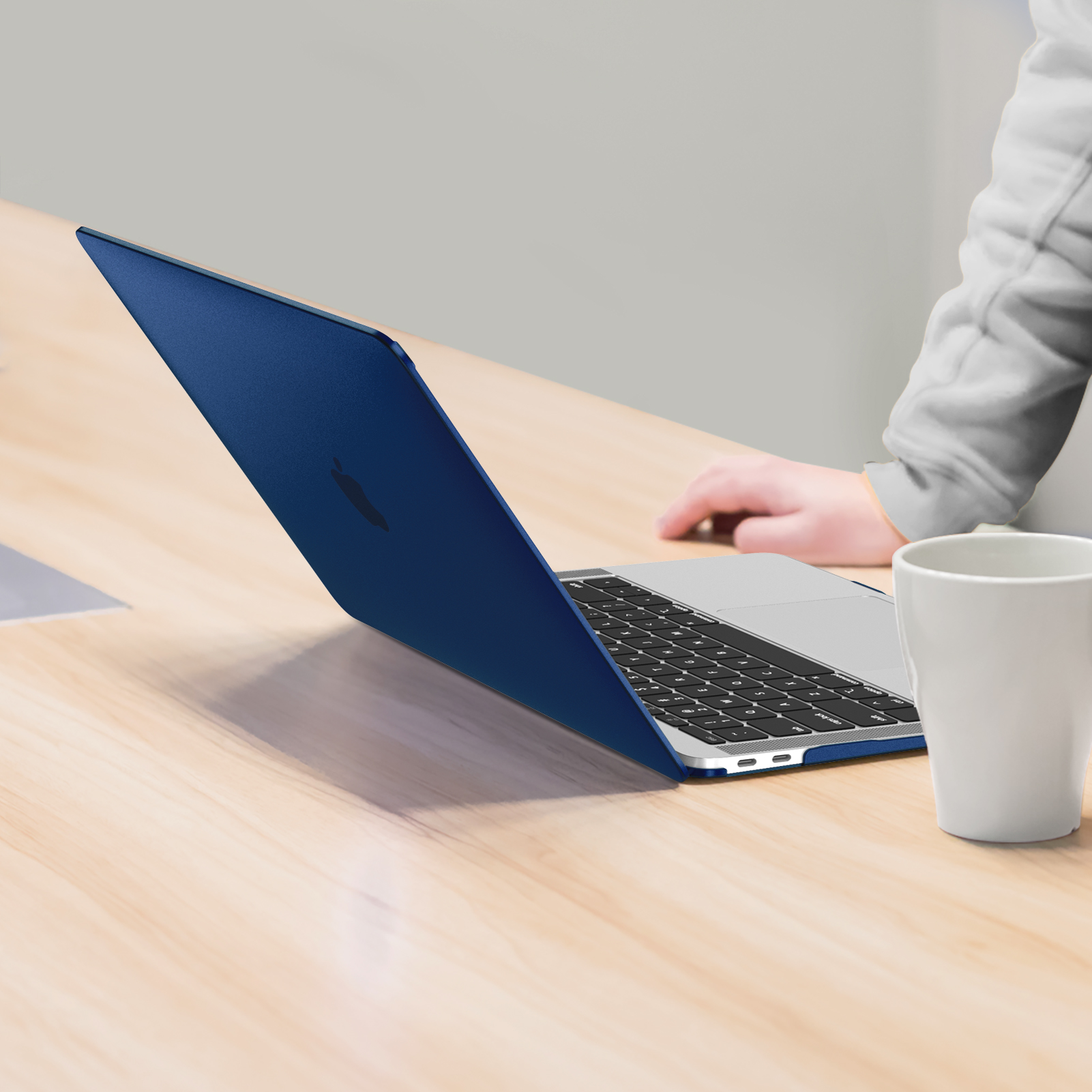 Blauer Laptop offen auf einem Holztisch. Ein weißer Becher steht in der Nähe des Laptops auf dem Tisch.