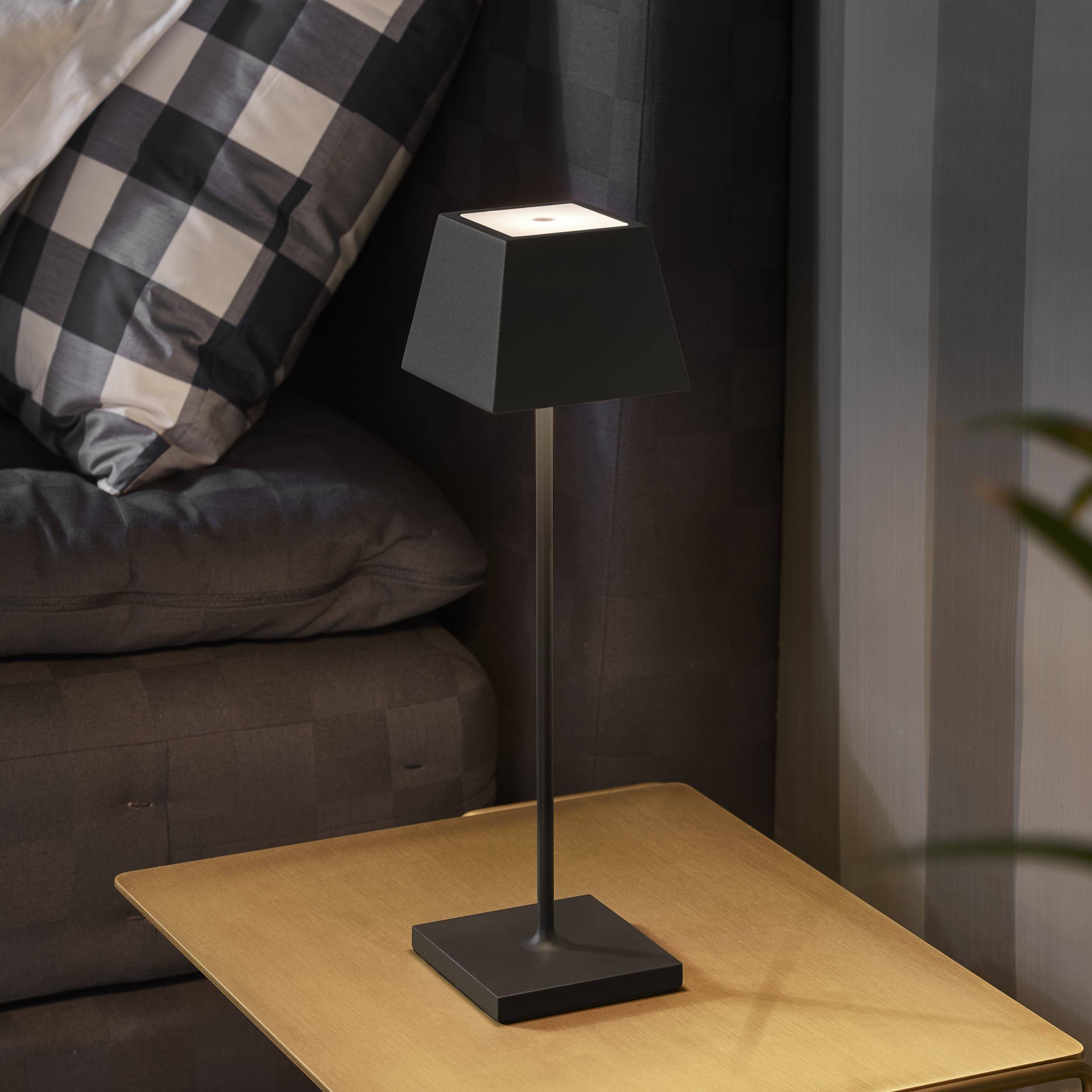 Schwarze Tischlampe mit quadratischem Fuß und Schirm, auf einem goldenen Tisch.
