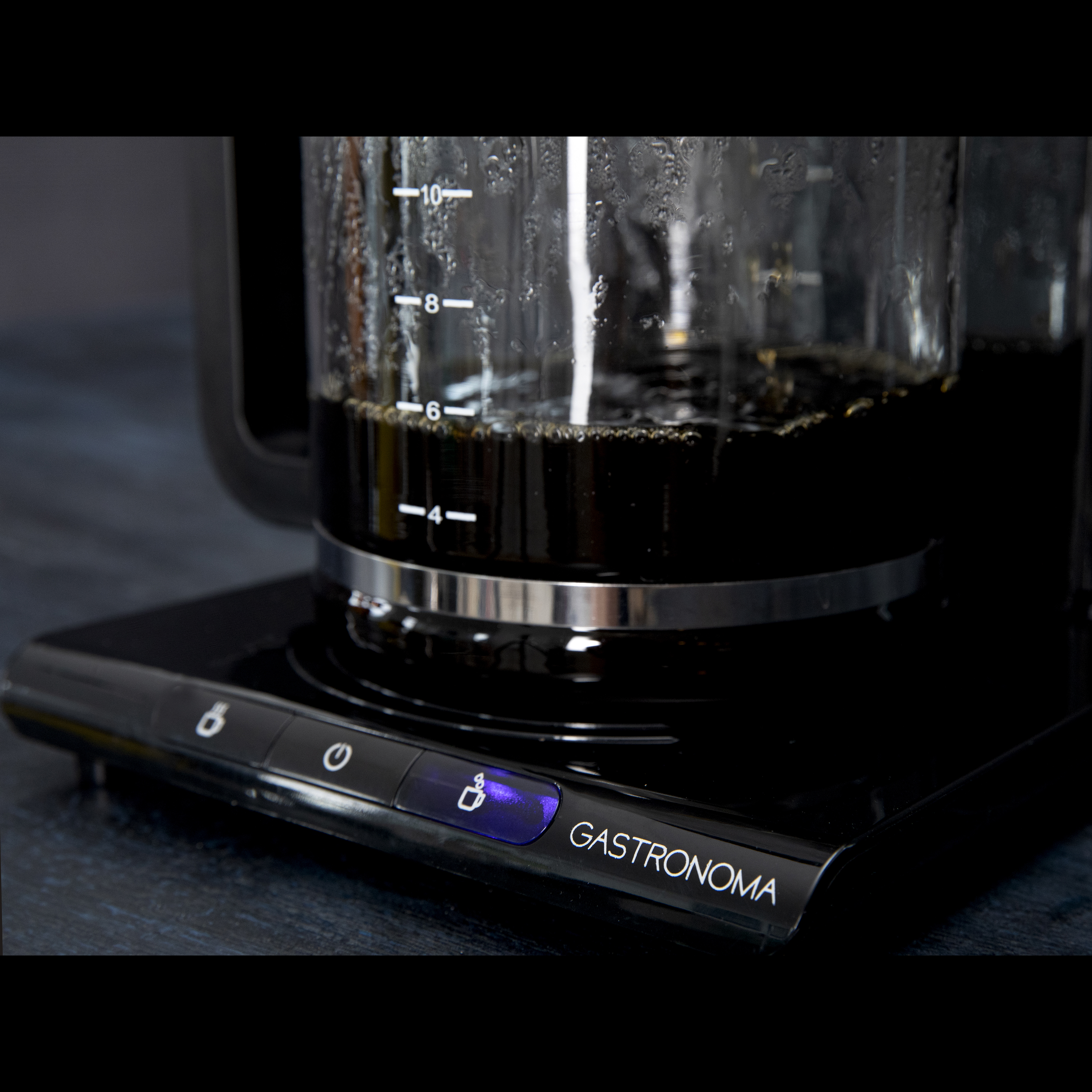 Black coffee maker with a glass carafe filled with dark coffee. A blue light is on.