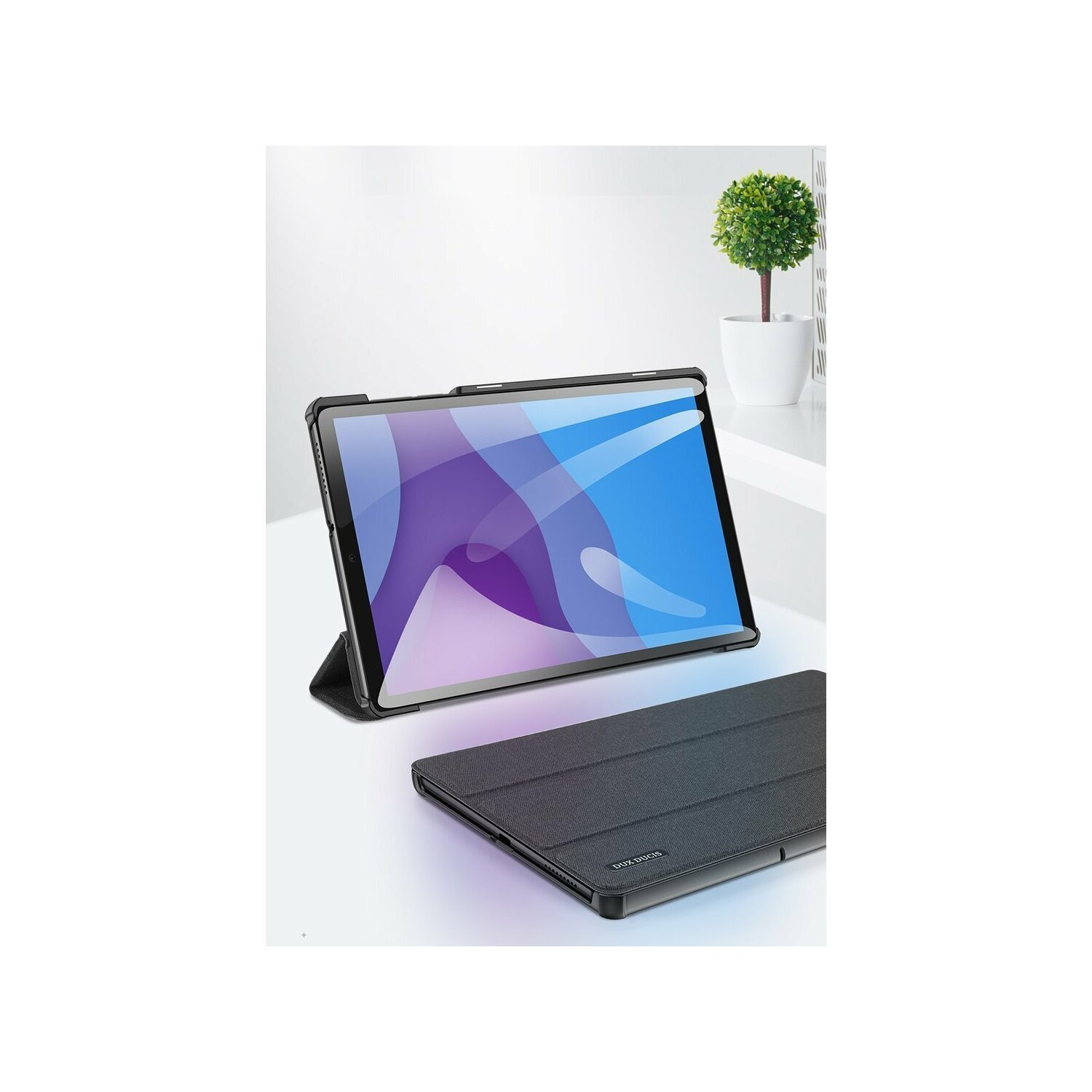 Ein Tablet in einer schwarzen Hülle liegt auf einer weißen Oberfläche. Im Hintergrund steht eine Topfpflanze. Eine Hülle liegt offen.