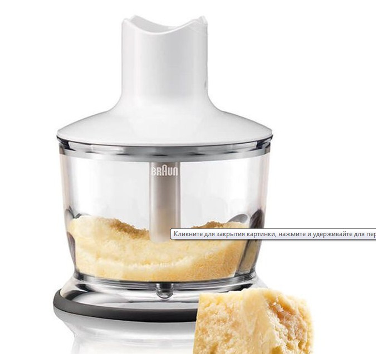 Una batidora de mano Braun blanca con un recipiente transparente que contiene comida y un trozo de queso parmesano.