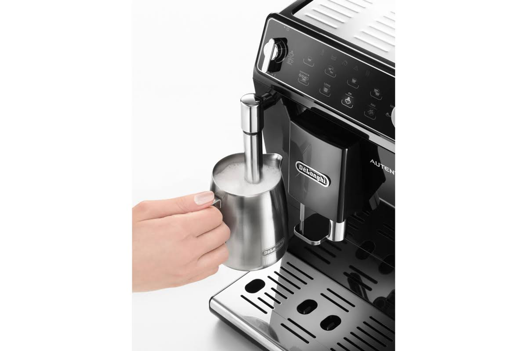 Een hand schenkt melk in een kopje onder een zwart-zilveren espressomachine.