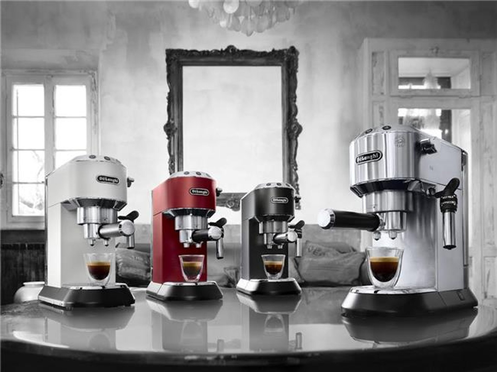Cztery ekspresy do espresso w różnych kolorach na stole, z filiżankami do kawy.