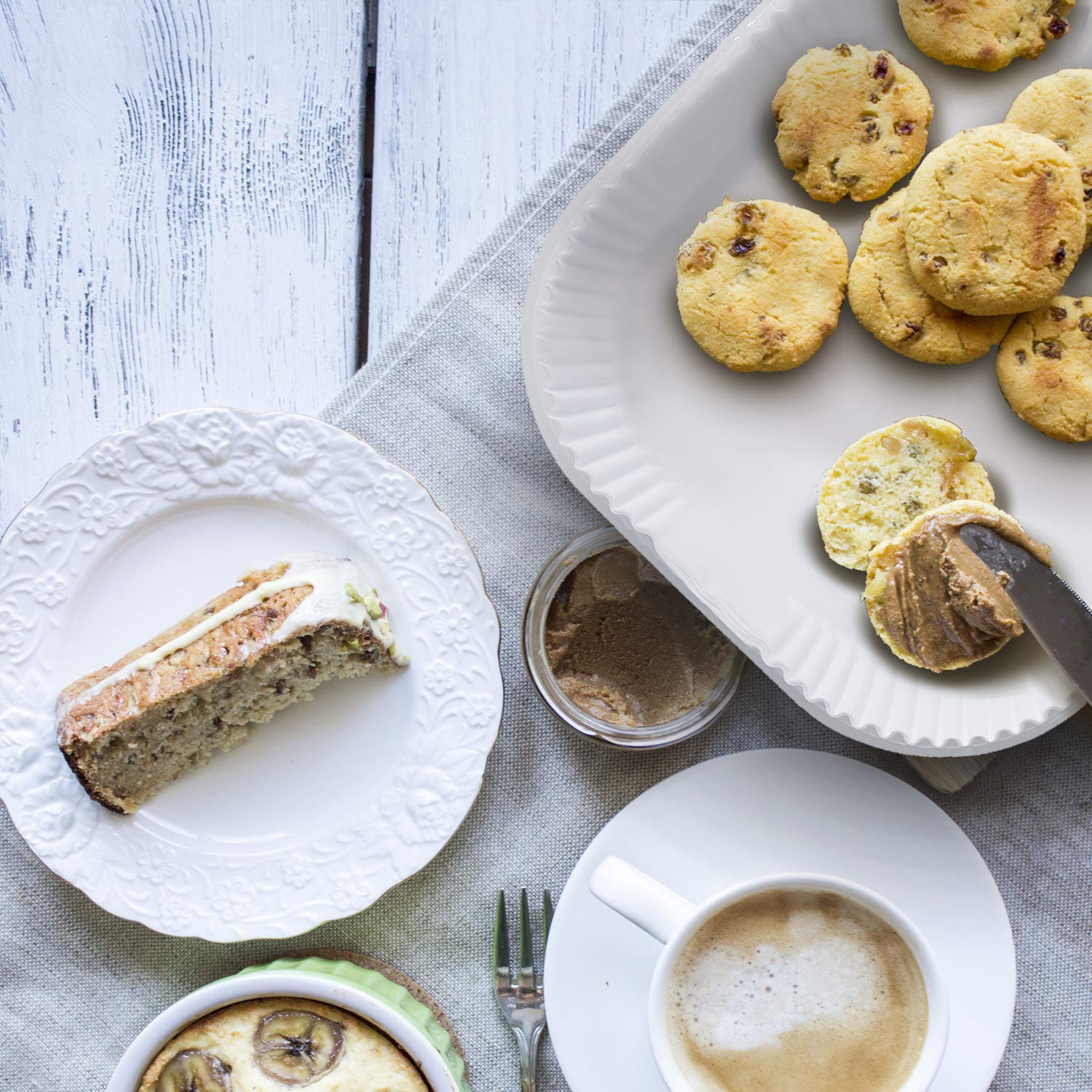 Draufsicht auf Frühstück mit Keksen, Kuchen, Kaffee und Aufstrich auf einem Holztisch.