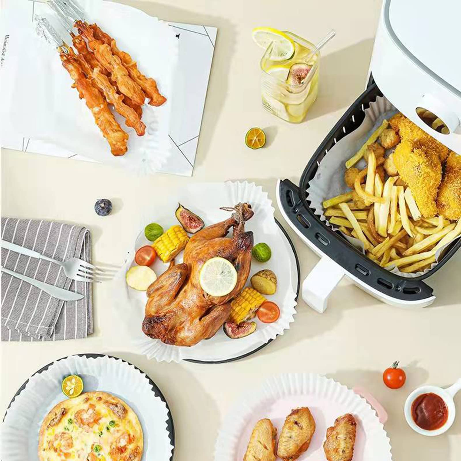 Ein Tisch mit gekochtem Essen: Hähnchen, Pommes, Pizza und Spieße, neben einer Heißluftfritteuse.