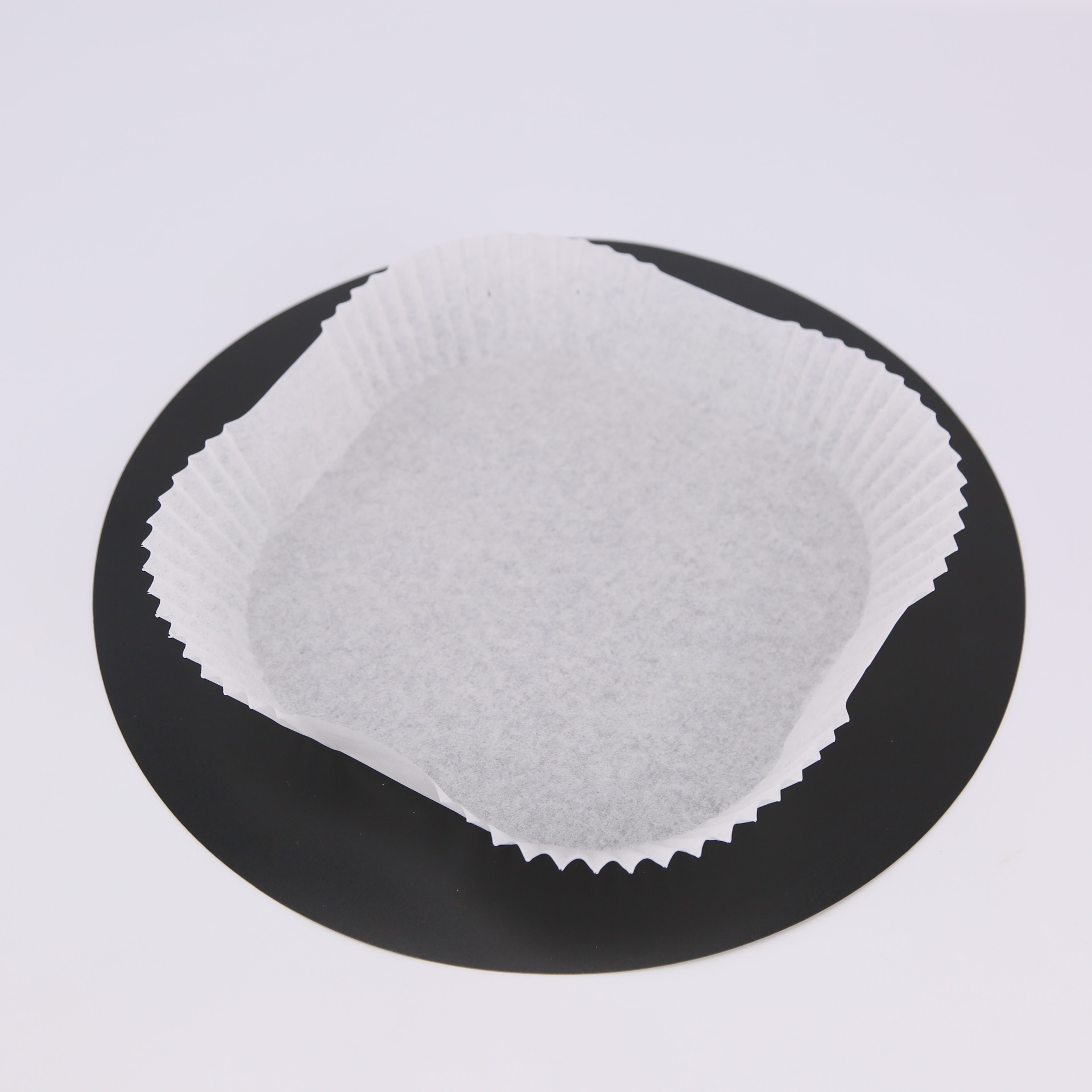Eine weiße Papier-Cupcake-Form in einer schwarzen, runden Backform auf weißem Untergrund.