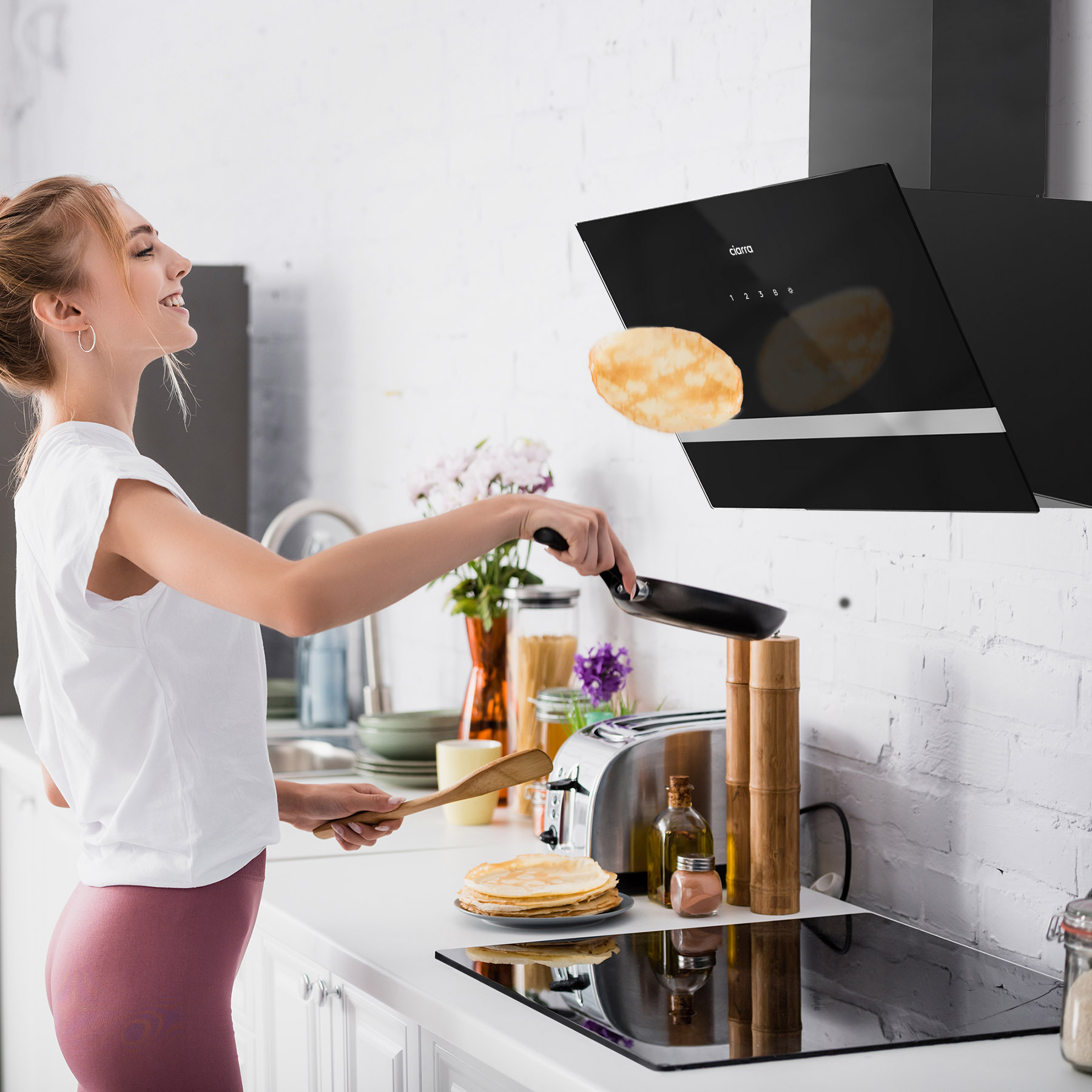 Frau, die in einer Küche einen Pfannkuchen wendet. Über ihr eine Dunstabzugshaube, auf dem Tresen Pfannkuchen.