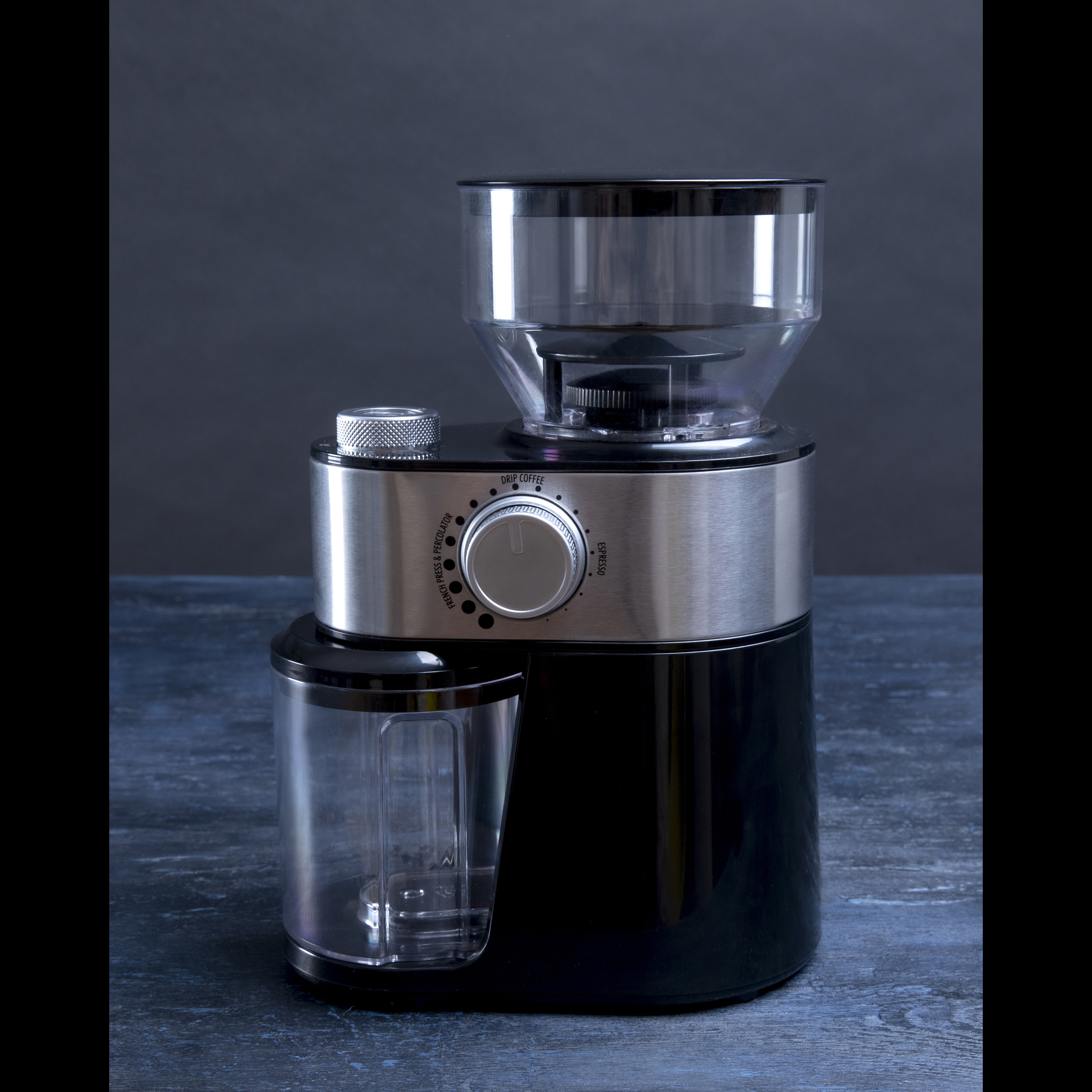 Młynek do kawy w kolorze czarnym i srebrnym, z przezroczystym pojemnikiem i pokrętłem.