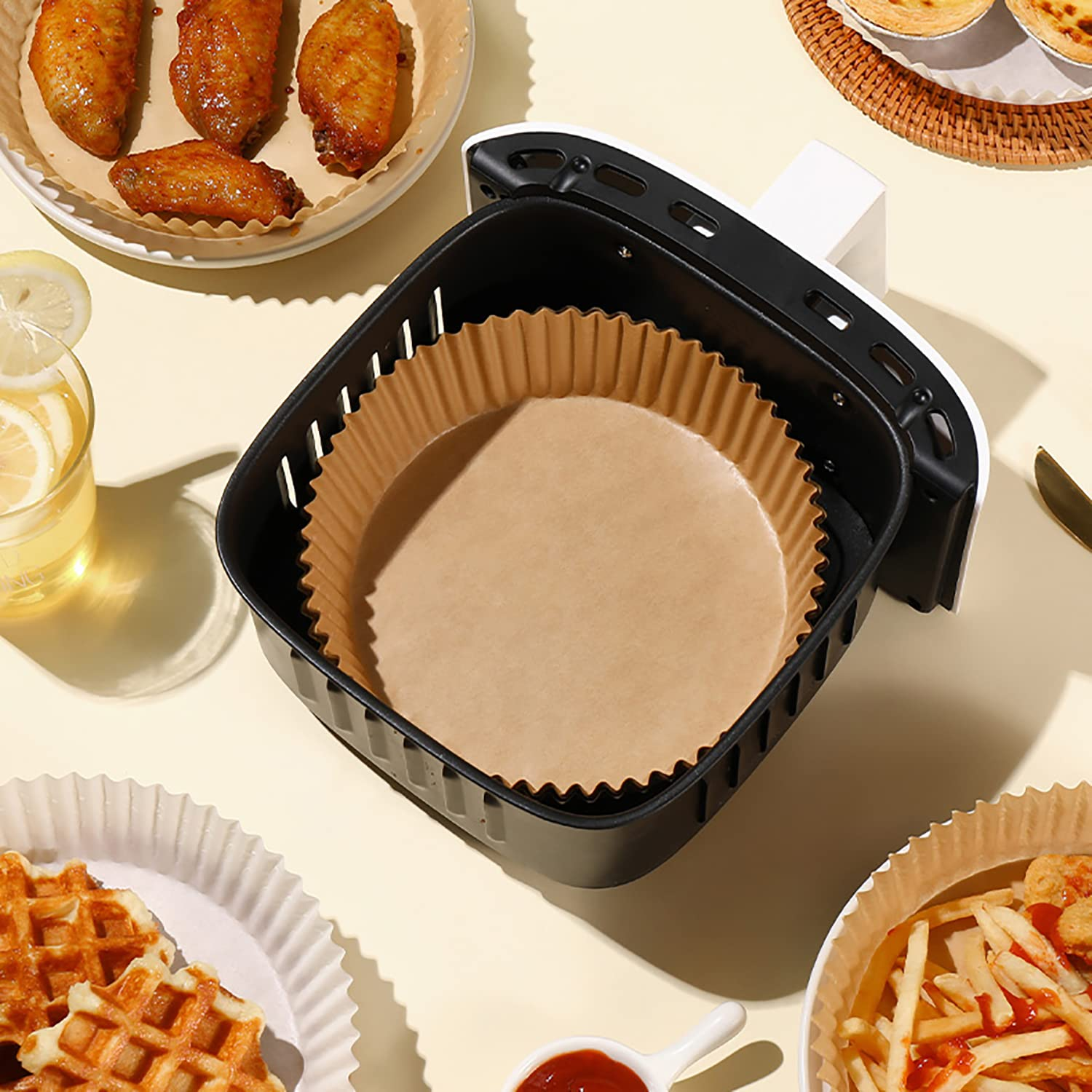Heißluftfritteuse mit Essen und Papiereinlagen. Waffeln, Flügel und Pommes sind sichtbar.