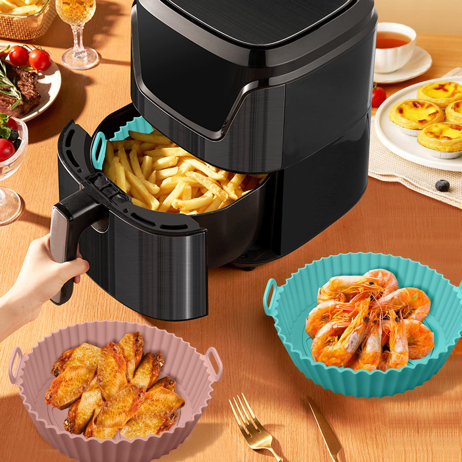 Heißluftfritteuse mit Essen, Pommes, Garnelen und Hähnchenflügeln in farbigen Silikonbehältern.