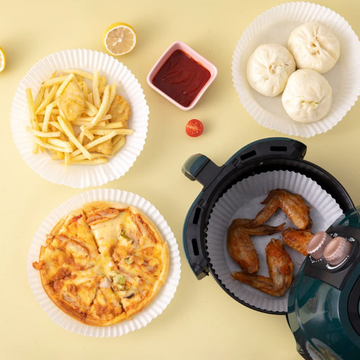 Heißluftfritteuse mit Essen: Pommes, Pizza, Chicken Wings und Brötchen in Papiereinlagen, mit Ketchup und Zitrone.