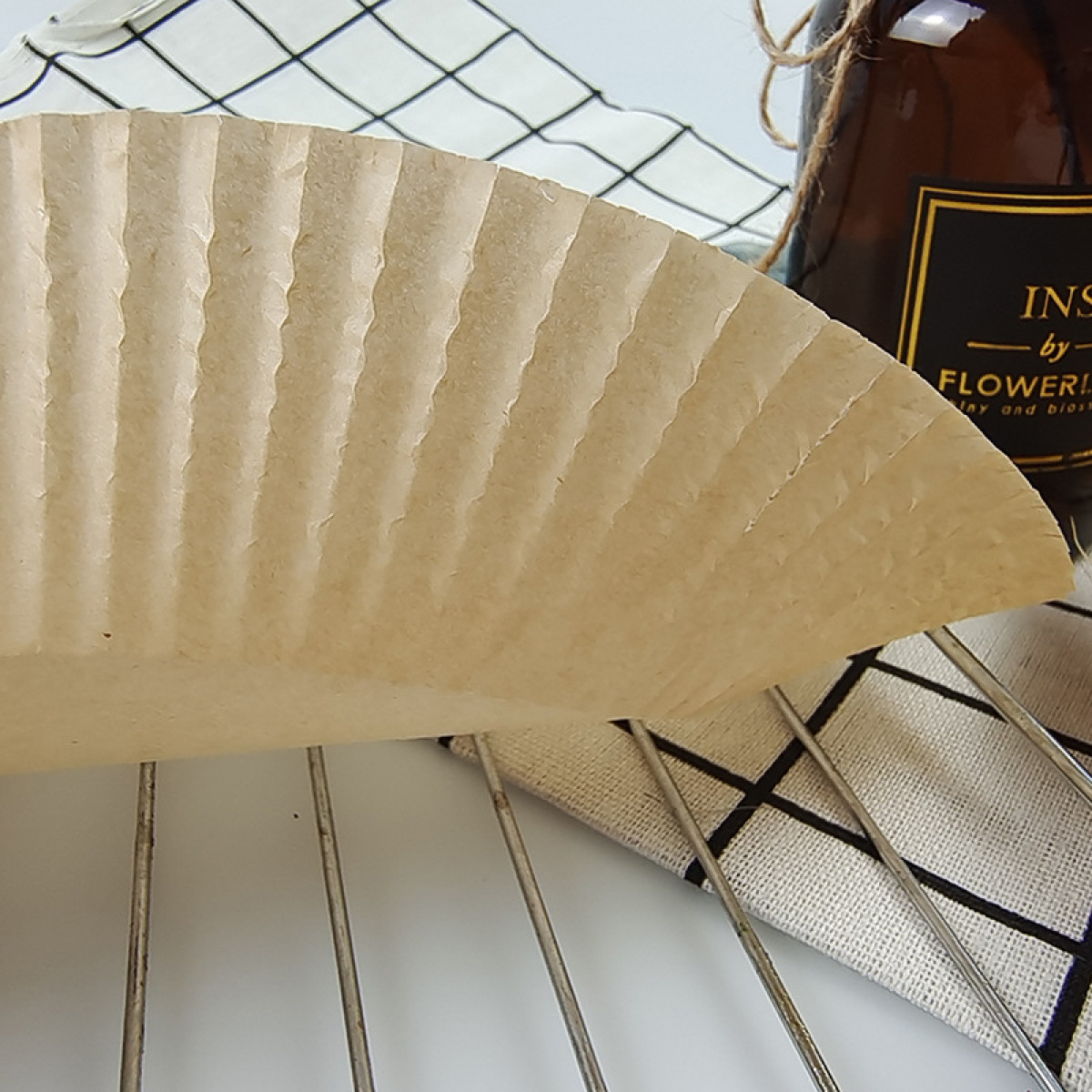 Papier-Backförmchen auf einem Drahtgestell, mit Flasche und Tuch im Hintergrund.