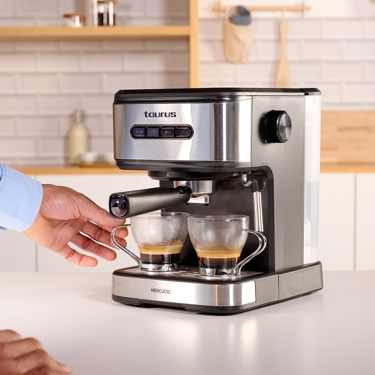 Ekspres do espresso z dwiema filiżankami kawy. Ręka trzyma filiżankę. Białe tło.